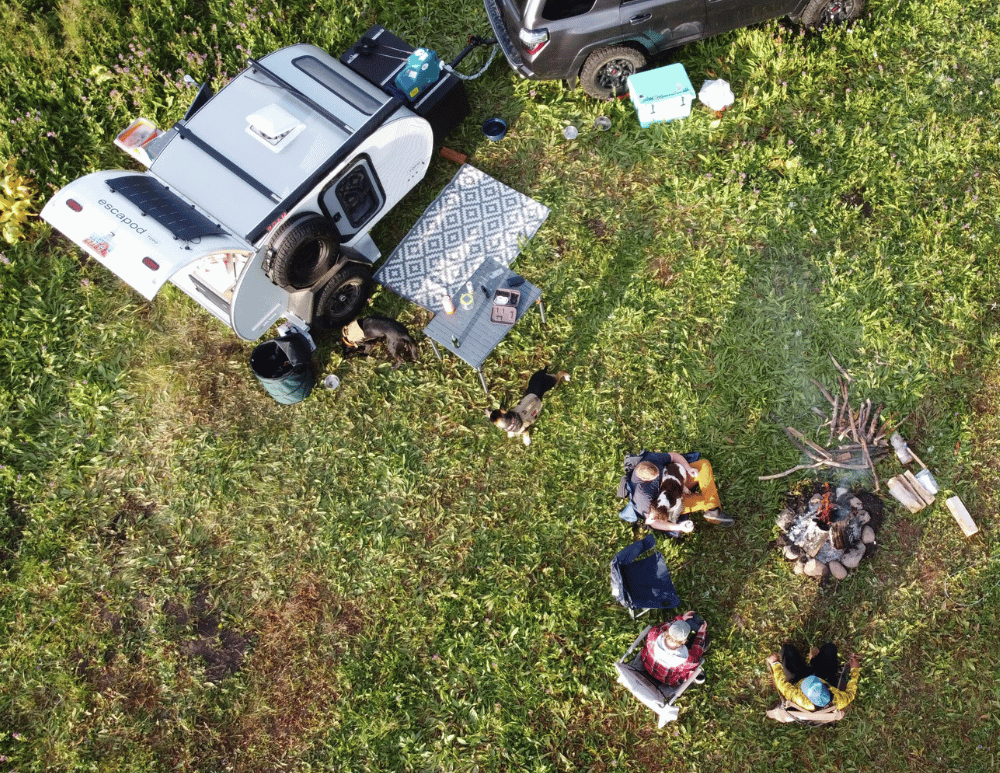 A bird's eye view of an Original TOPO trailer set up at camp with people sitting around a fire enjoying their camping experience.
