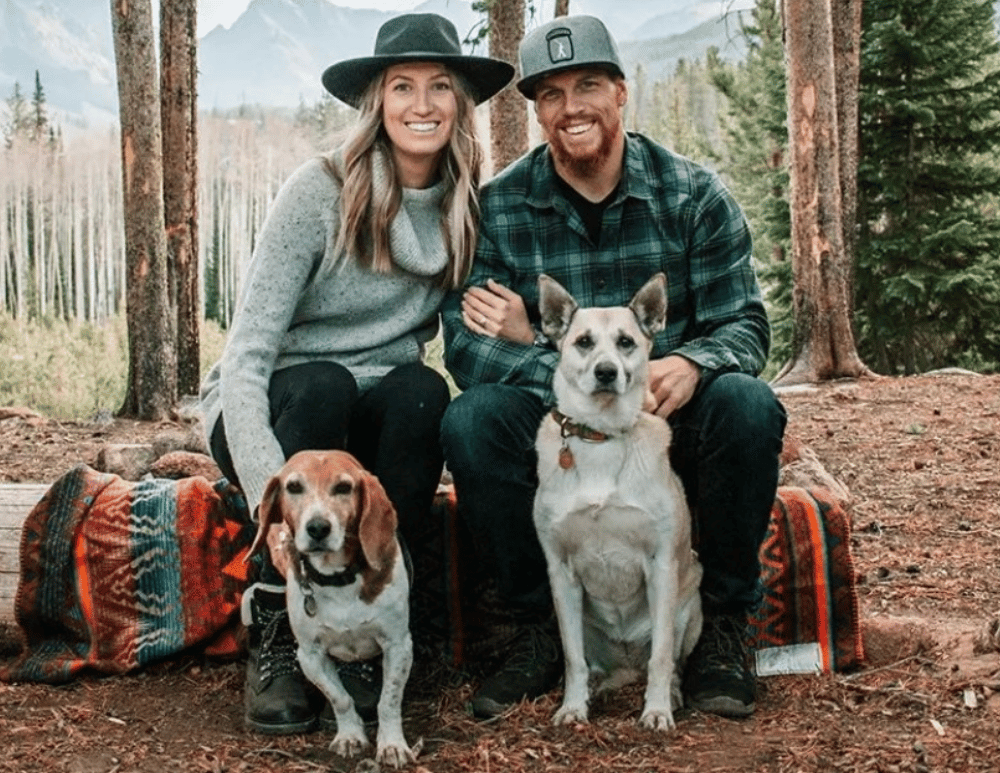 A couple sitting on a log posing with their two dogs for a familyphoto.