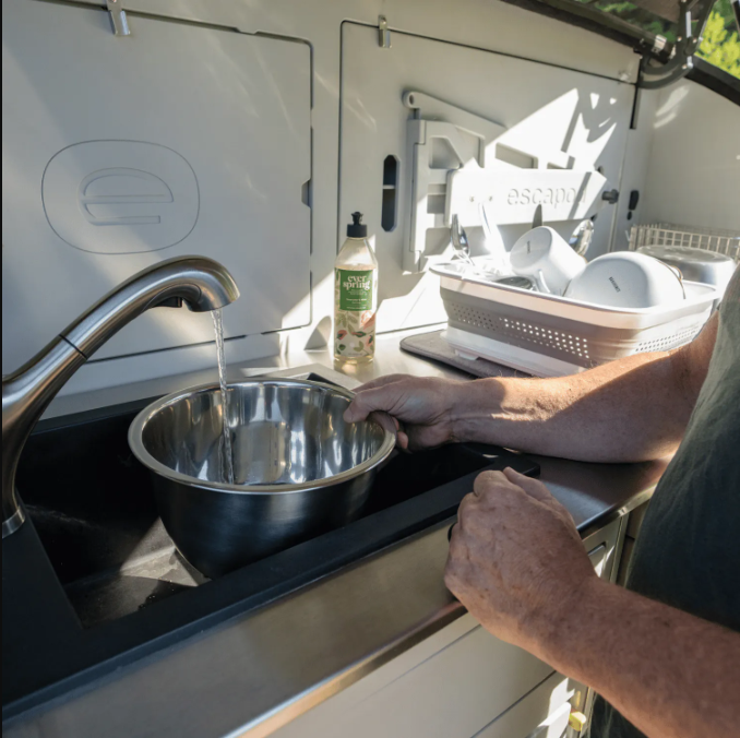 The sink is being used to wash all the dishes from camp in a teardrop camper.