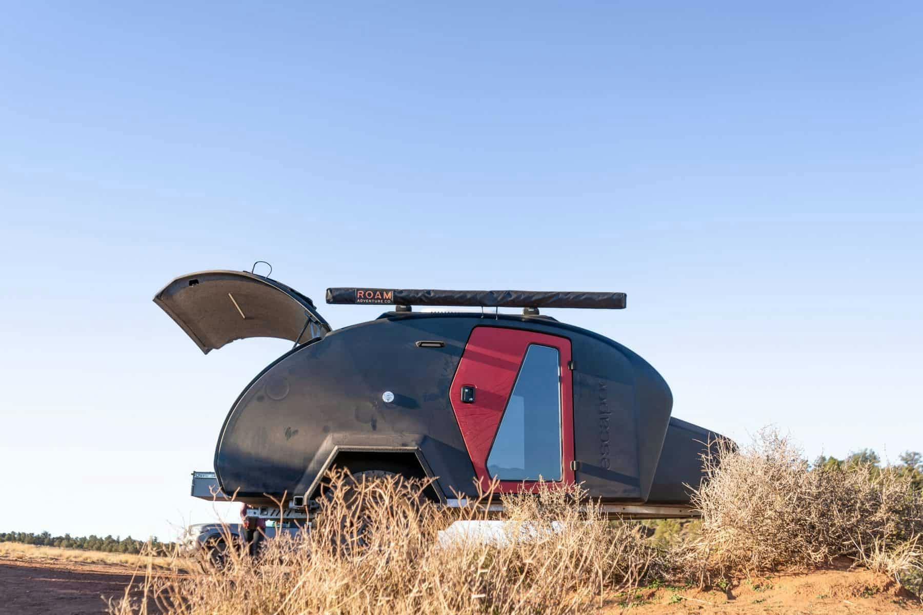 A navy blue teardrop camper with a red door, parked in a desert lanscape.