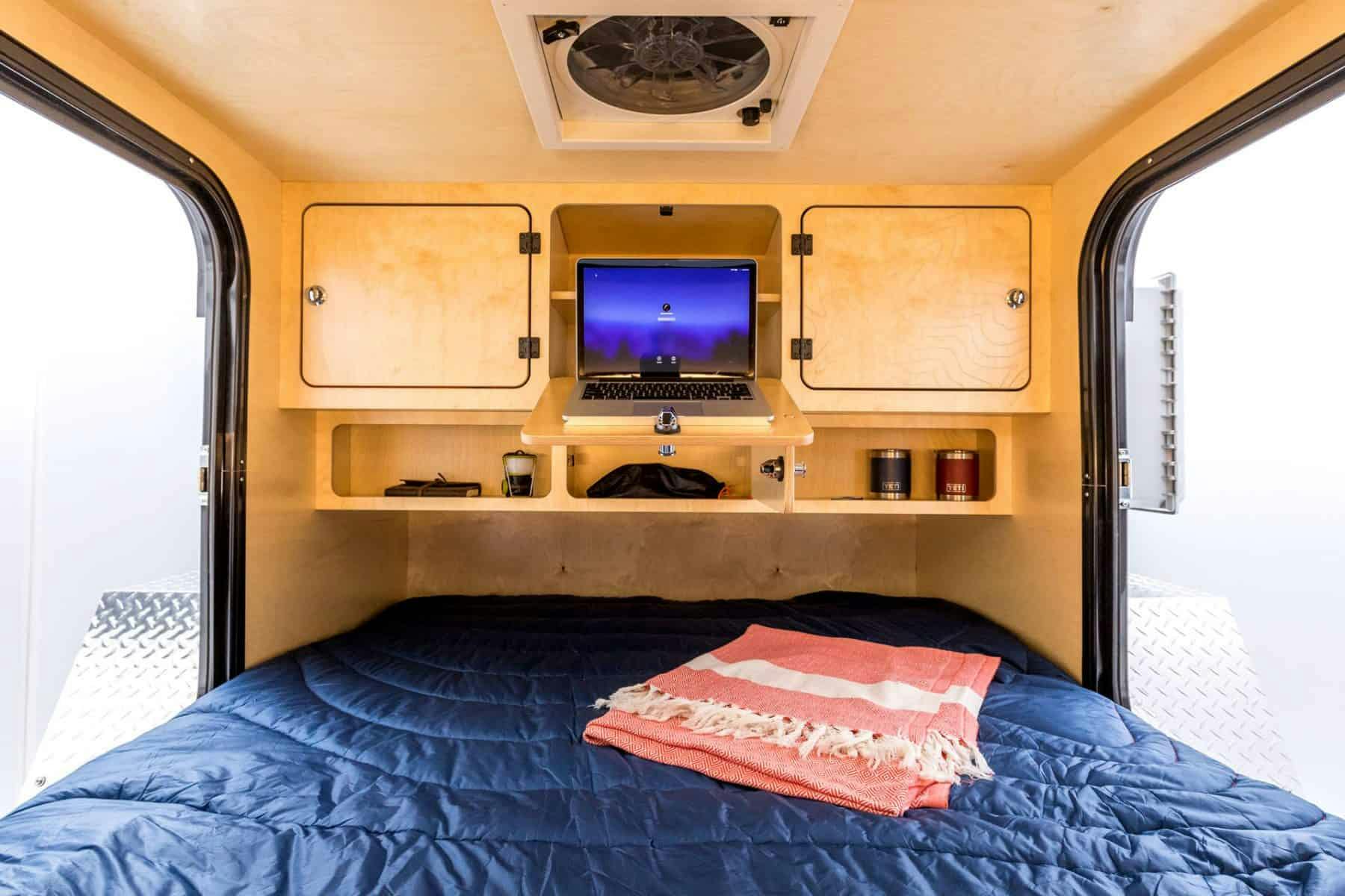 The interior to a teardrop camper, displaying beautiful birch cabinetry and a queen sized bed.