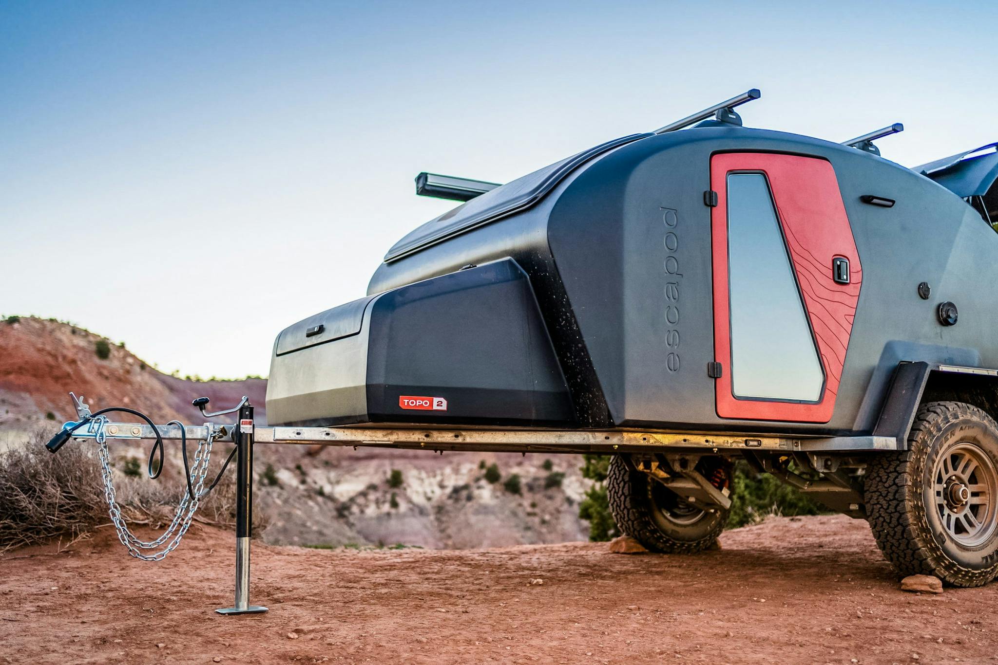 A navy blue teardrop trailer with a red door set up in a desert landscape for camping.