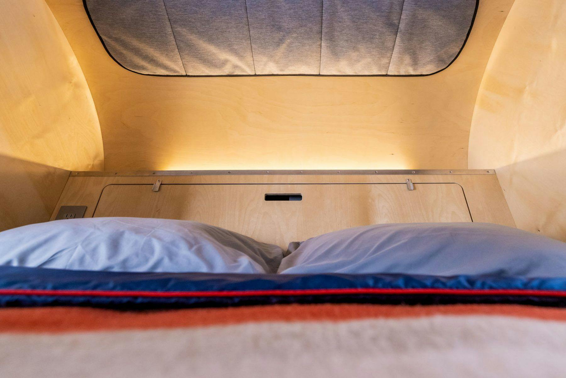 Birch interior of a teardrop trailer, showing a full queen size mattress, angled headboard, and stargazer window.