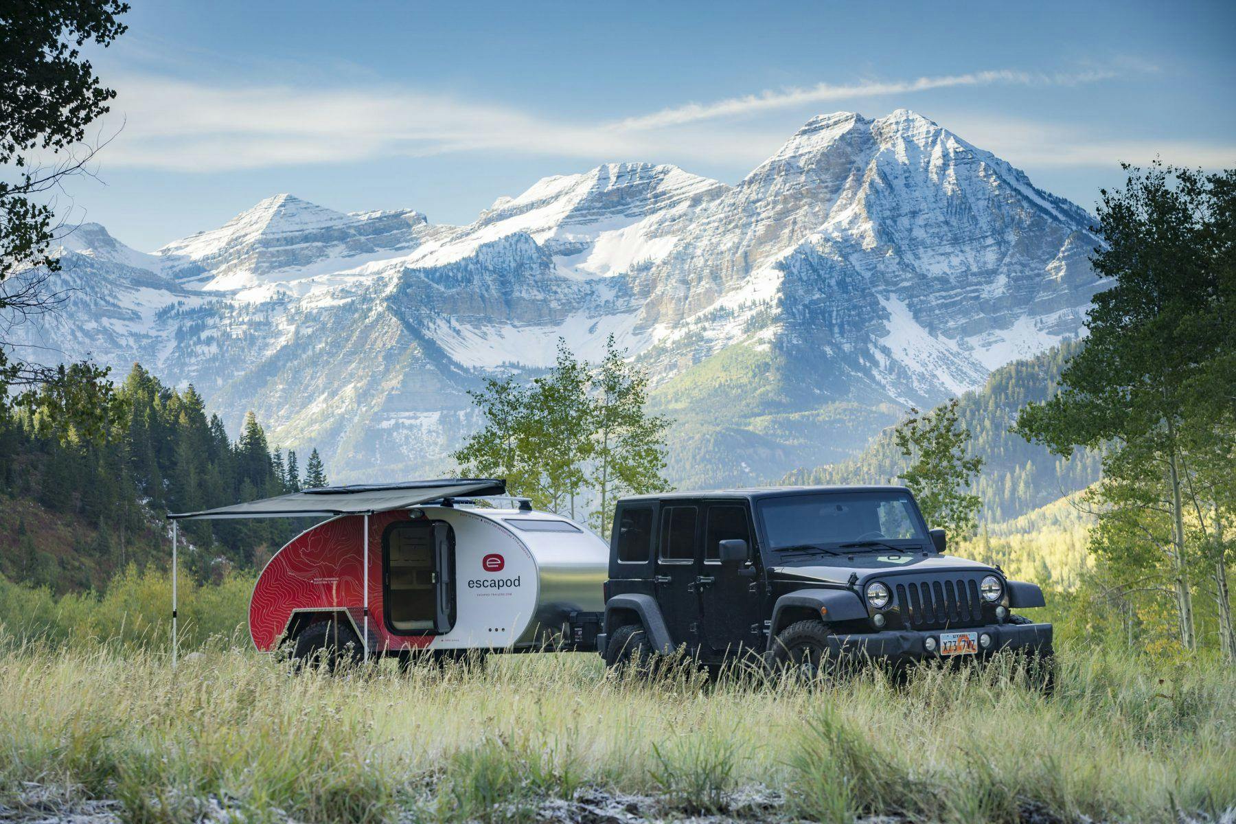 a teardrop camper being towed by a JEEP with a beautiful mountain range in the background.