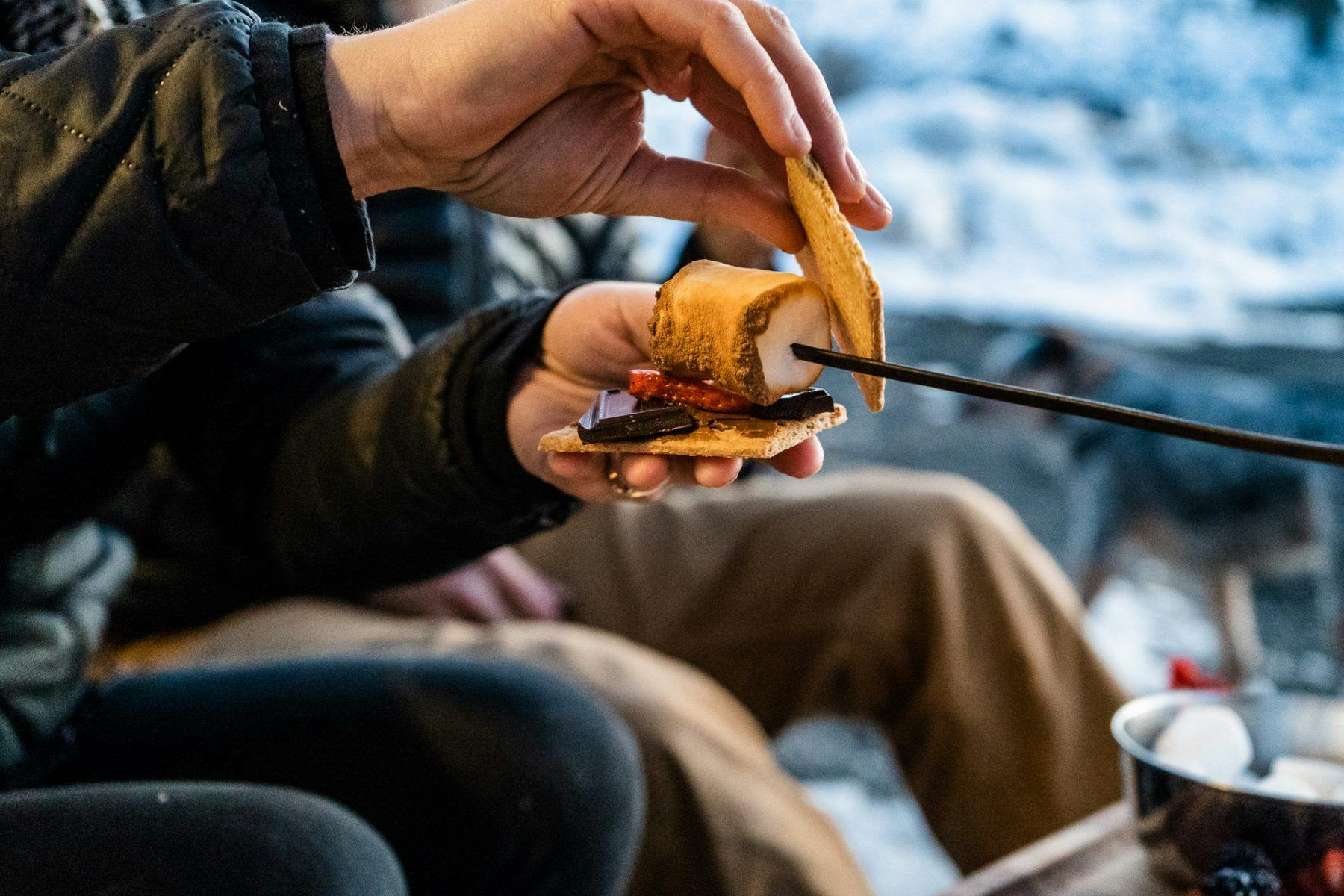 A woman squishing a smore into place around a campfire.