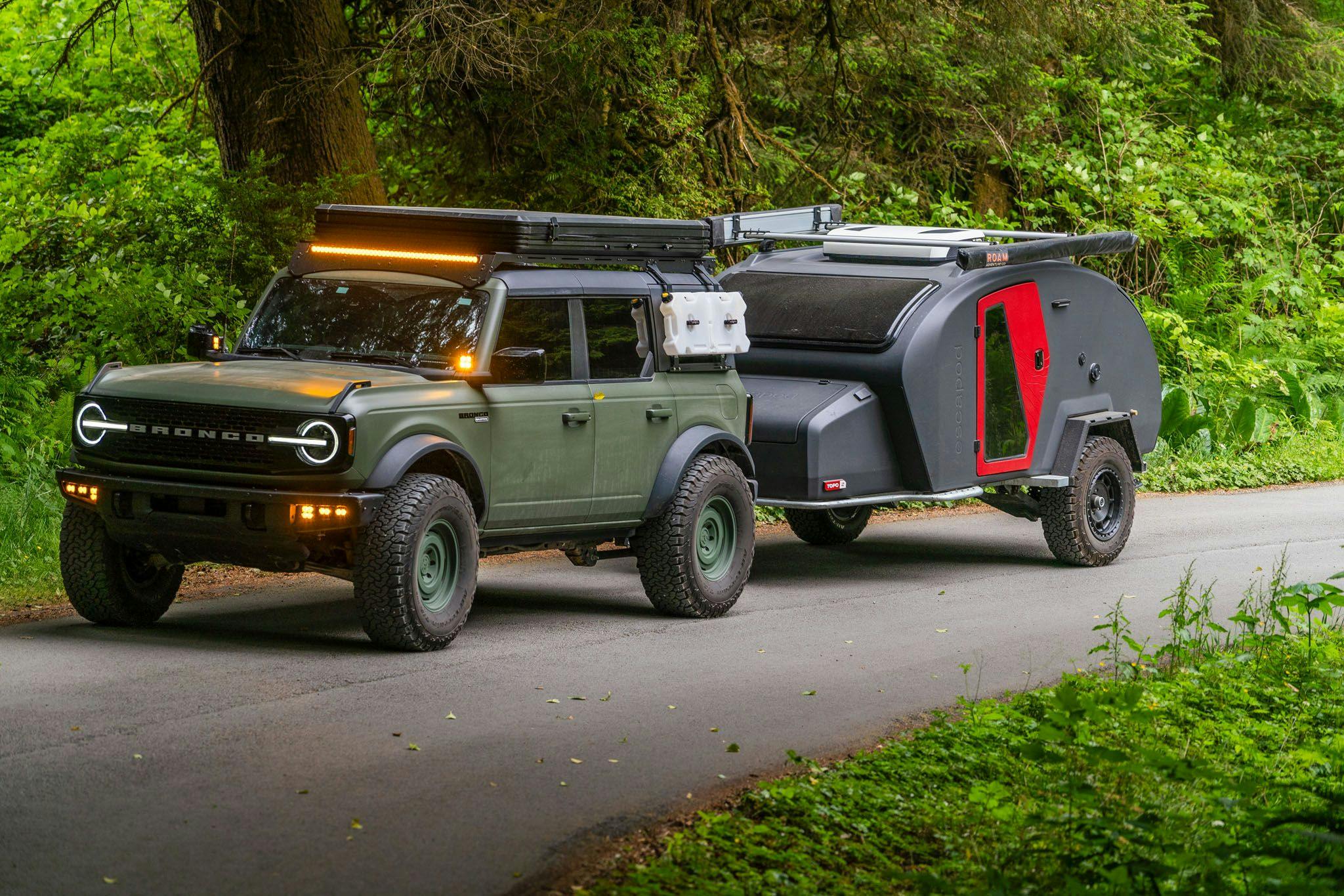 A TOPO2 being towed by a Ford Bronco through lush green foilage.