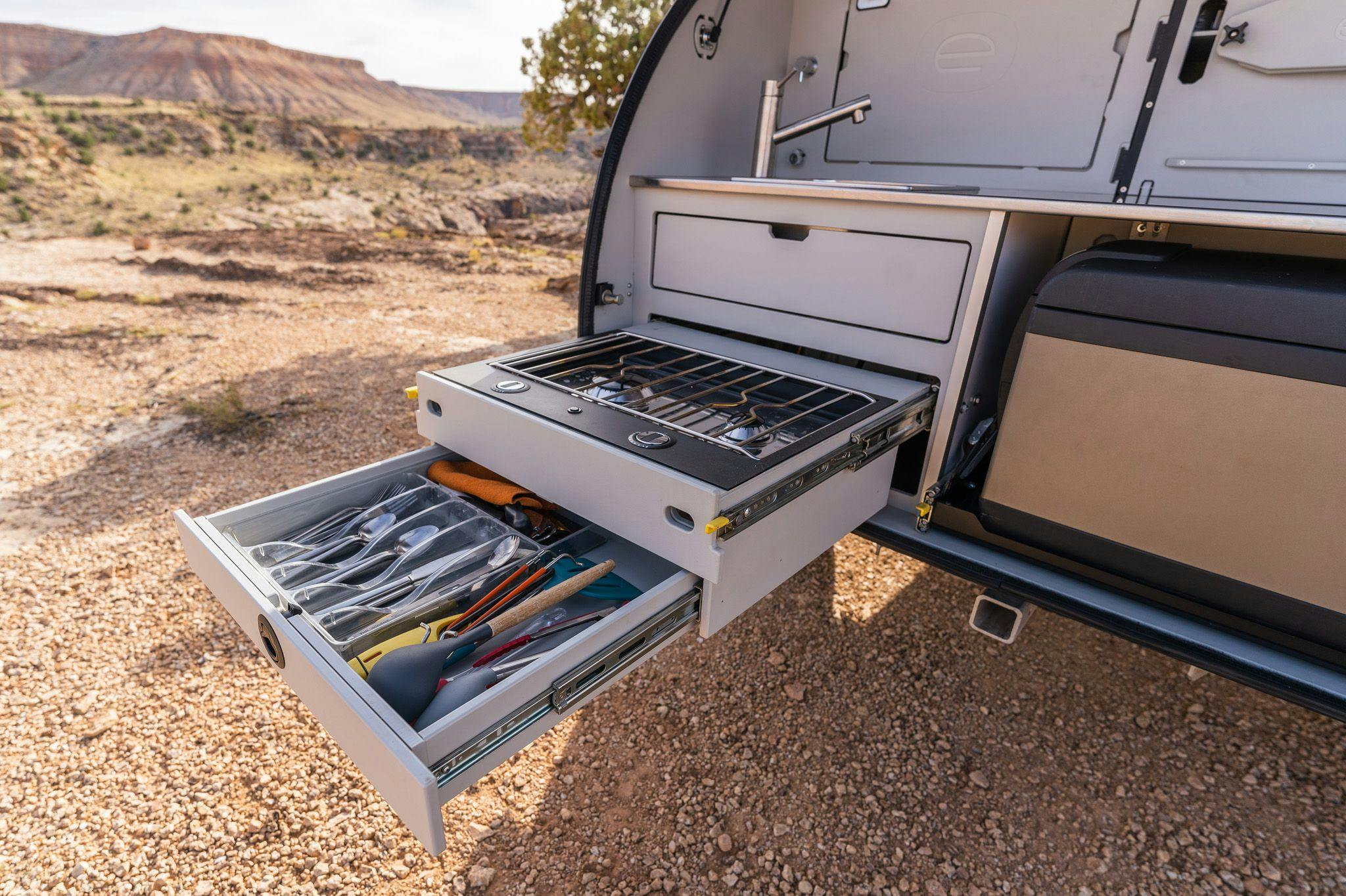 The camp kitchen in the TOPO2, an offroad trailer, showing a two burner stove, utensil drawer, sink, and more.