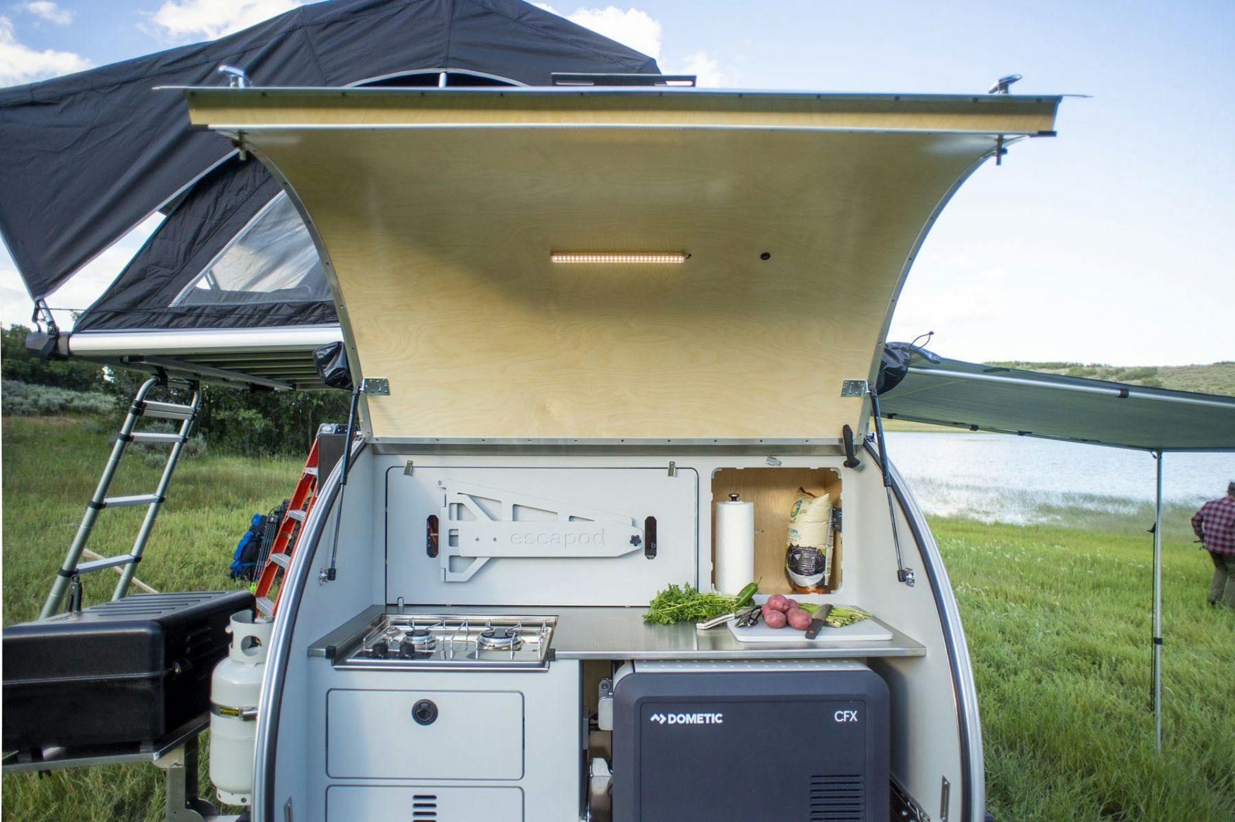 A teardrop trailer with the galley hatch opened revealing a camp kitchen for a weekend camping trip.