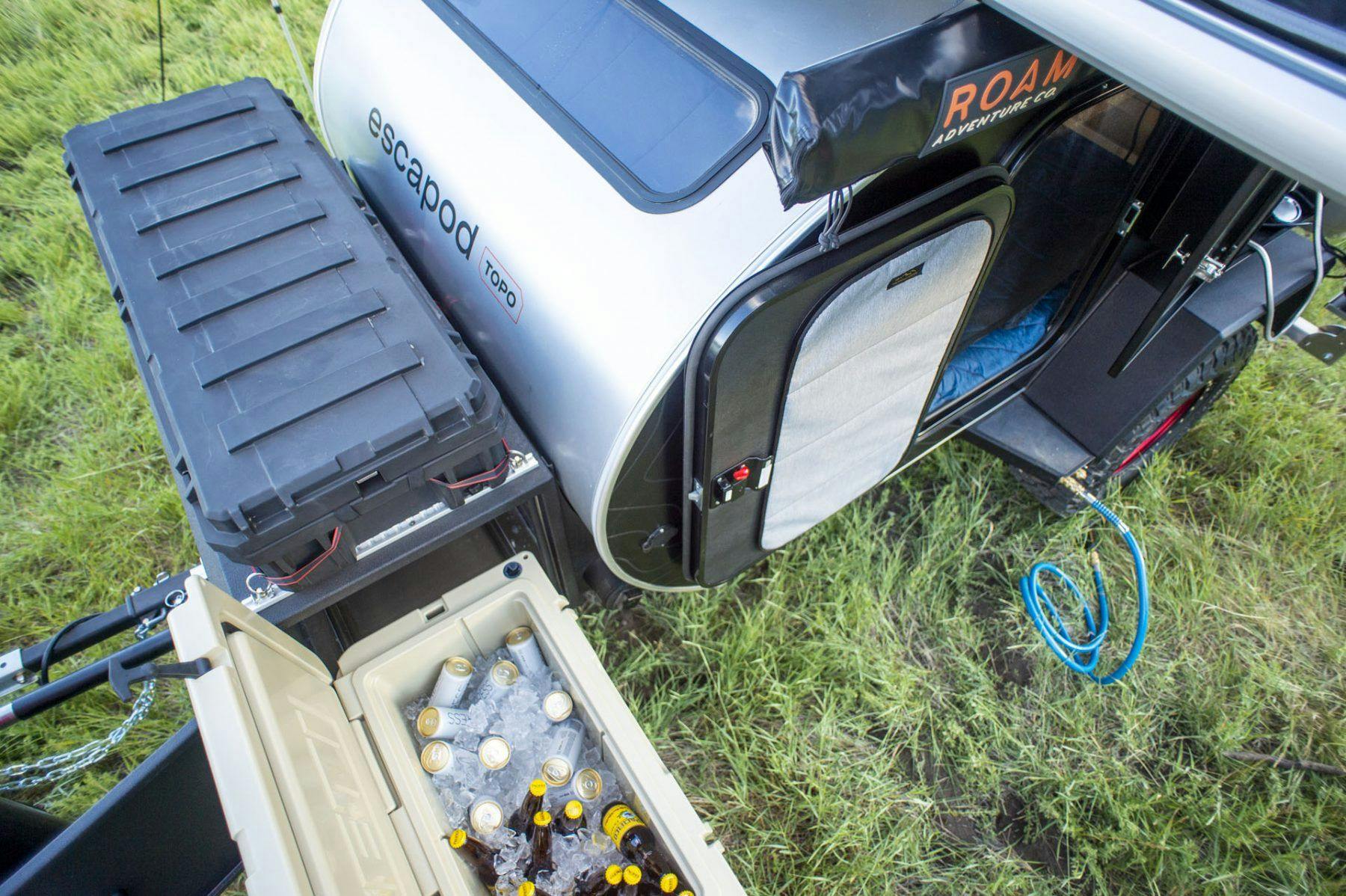 A teardrop trailer fully stocked with a cooler full of drinks for a weeknd of camping fun.