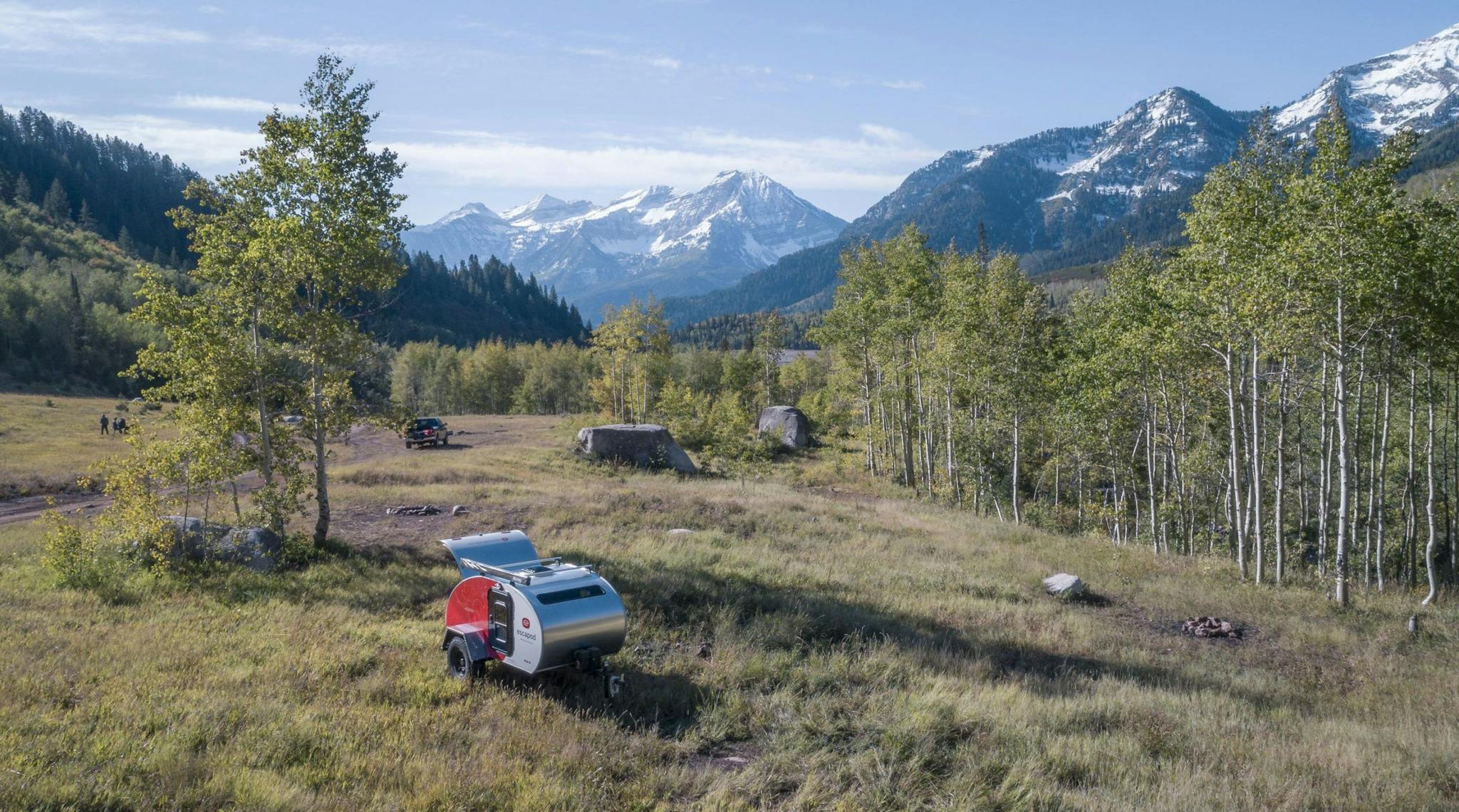 A white and red teardrop camper, in a remote area with trees and mountains in the background.