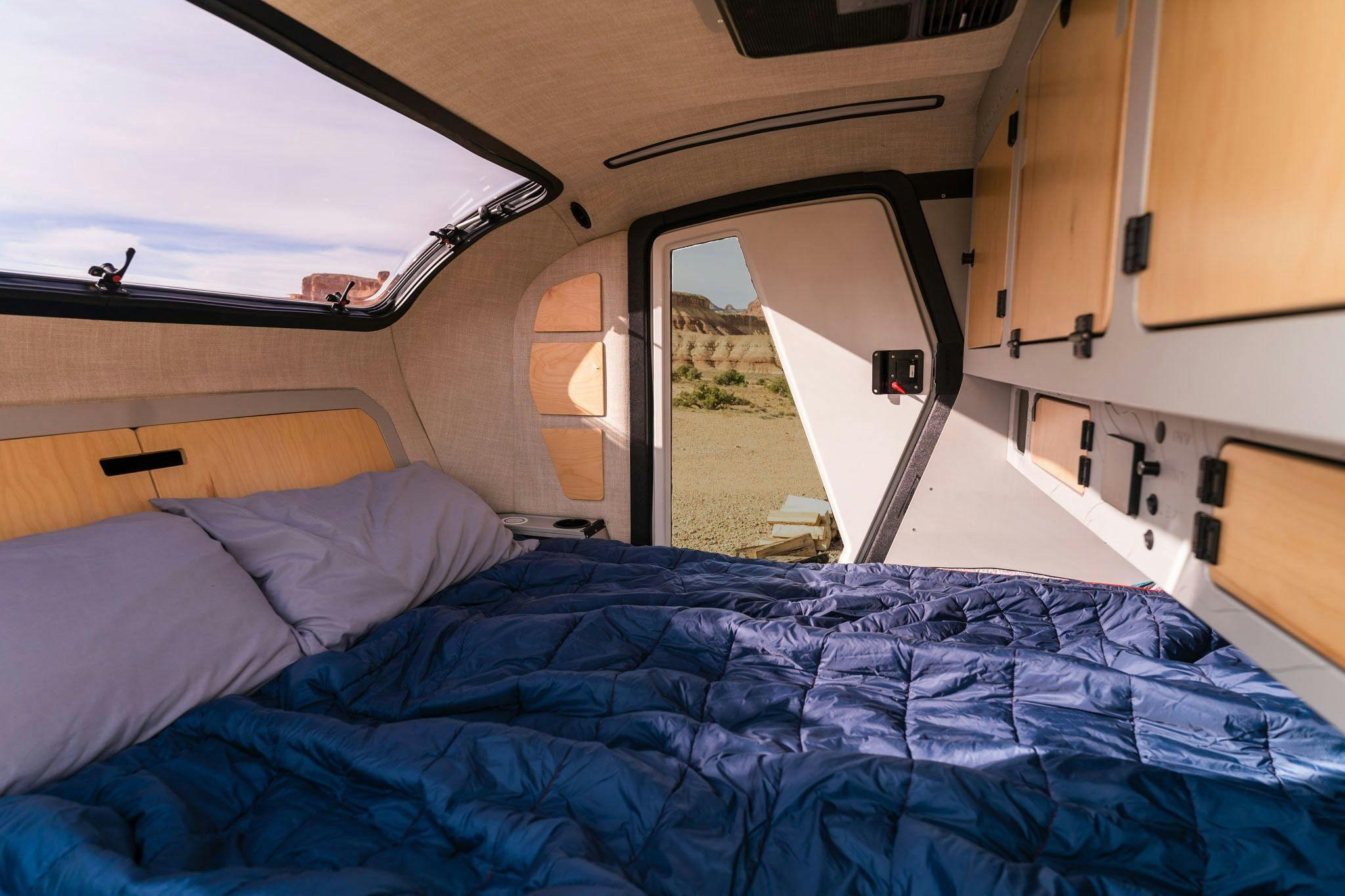 The interior of the TOPO2 Cabin, a teardrop trailer, that features a queen sized mattress, tons of storage, A/C, heat, and a stargazer window.