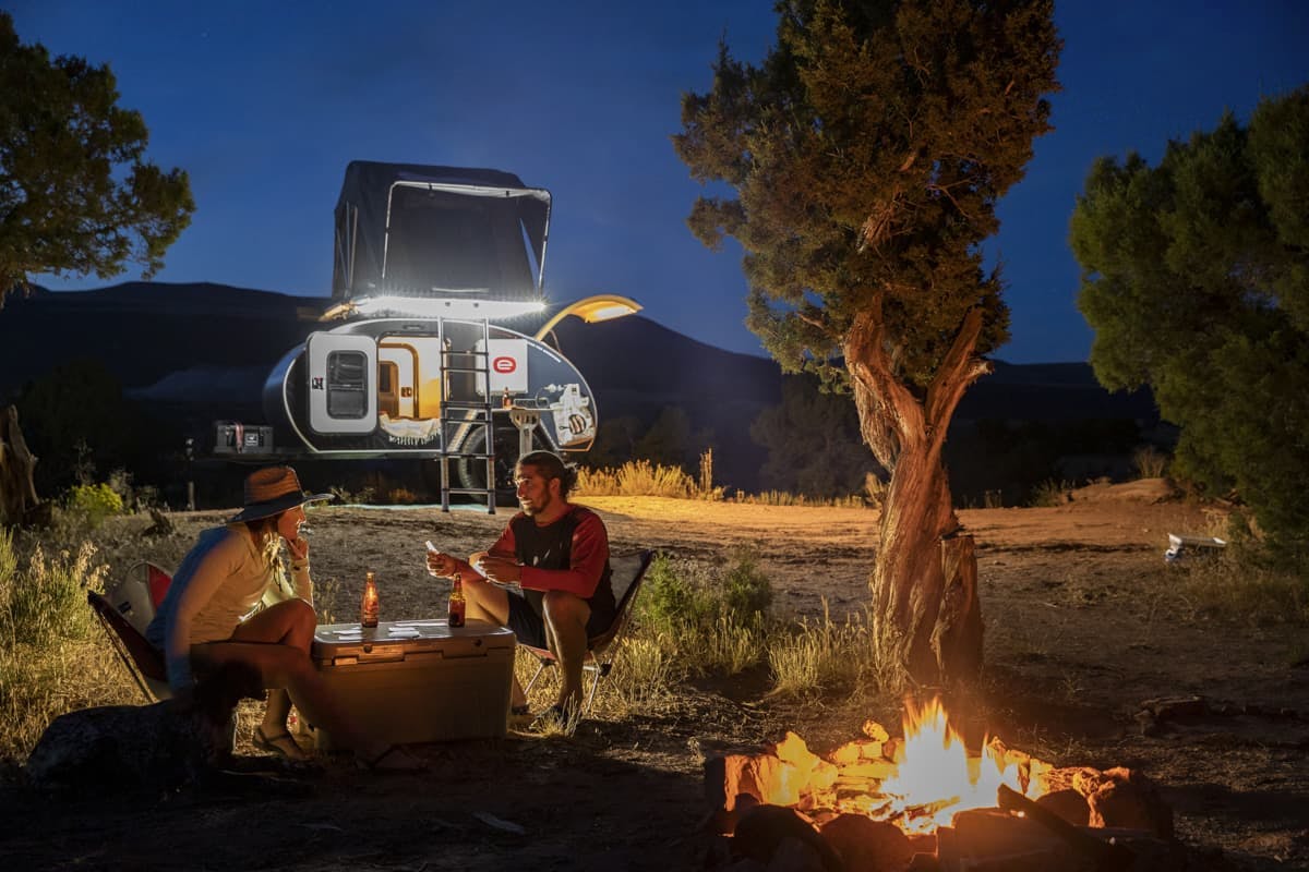 A couple enjoying time around the fire in front of their teardrop camper.