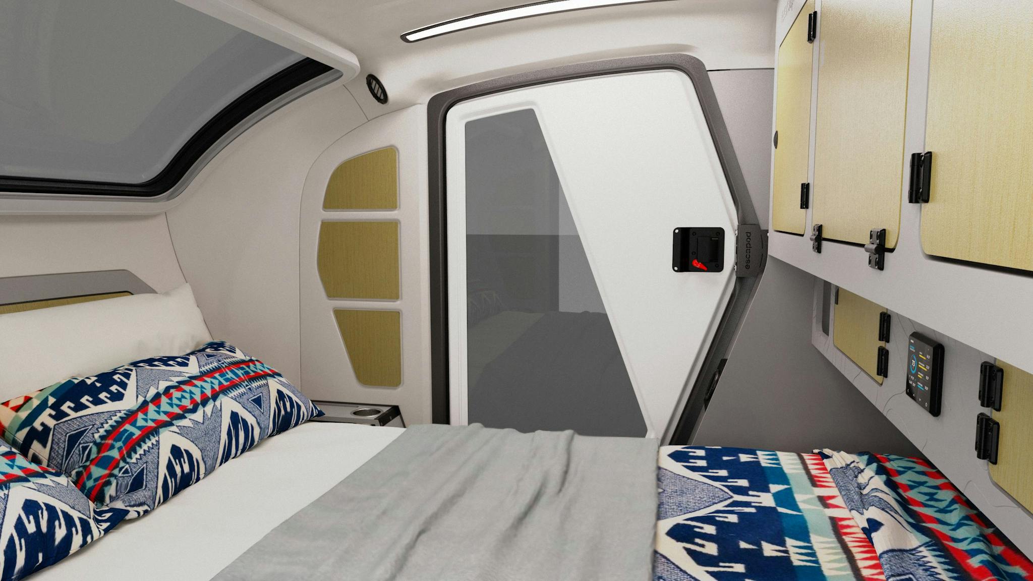 A look inside the cabin of the TOPO2 teardrop trailer. The queen-sized bed has a blue and red quilt covering it with a grey blanket in the middle.