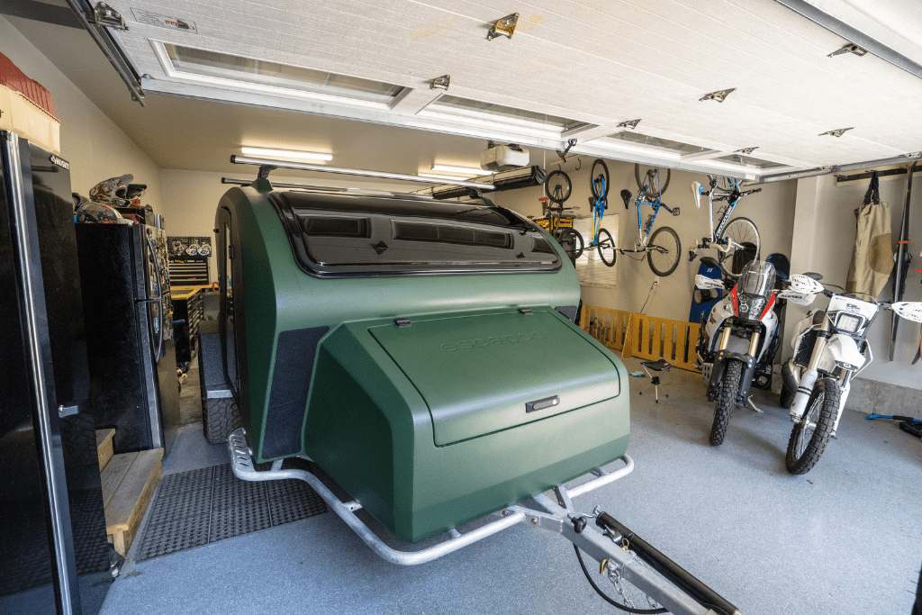A moss green TOPO2, offroad teardrop trailer is parked comfortably in a standard garage.