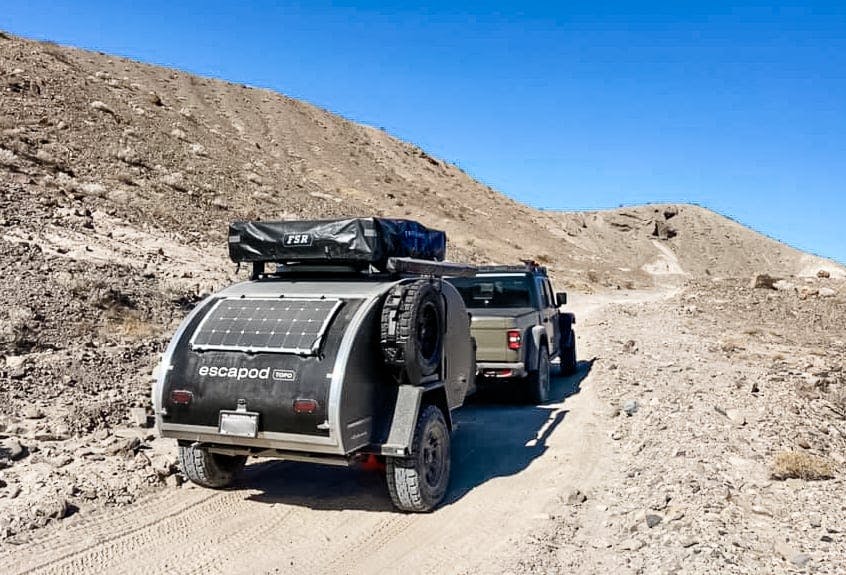 A black and grey teardrop trailer offroading on some rugged pathways.