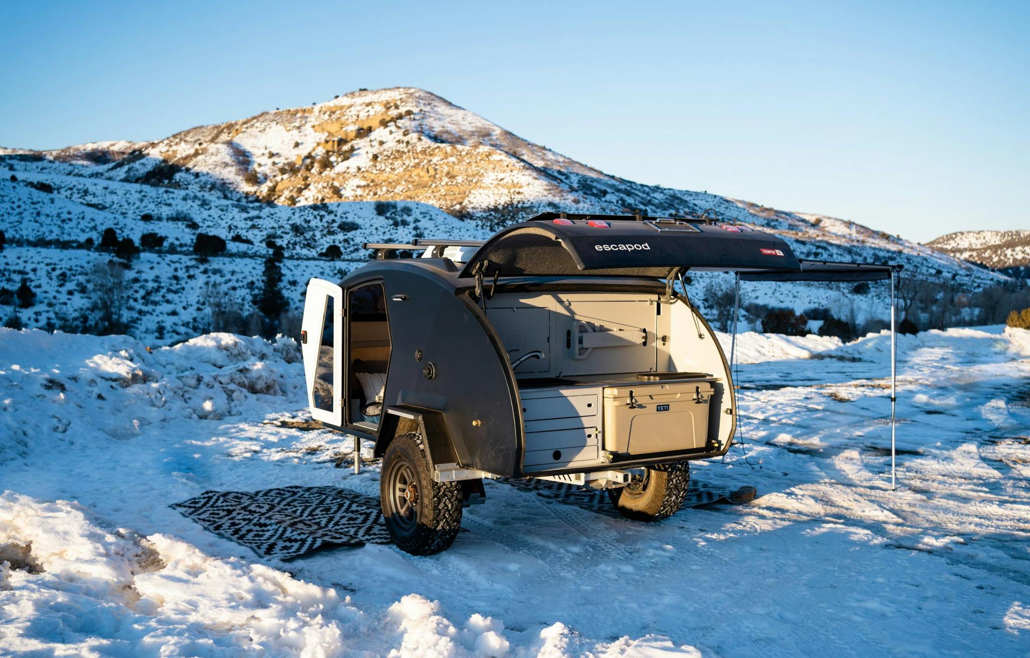 A navy blue teardrop camper parked in a winter landscape.