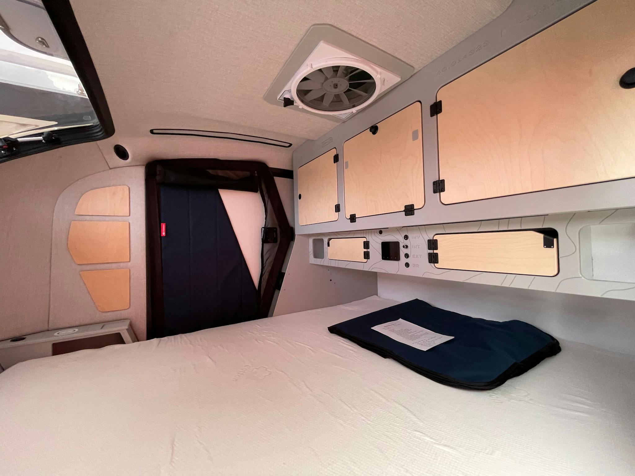 The cabin of a custom teardrop trailer by Escapod Trailers, displaying cabin storgage, night stands, and a Maxx Airfan.