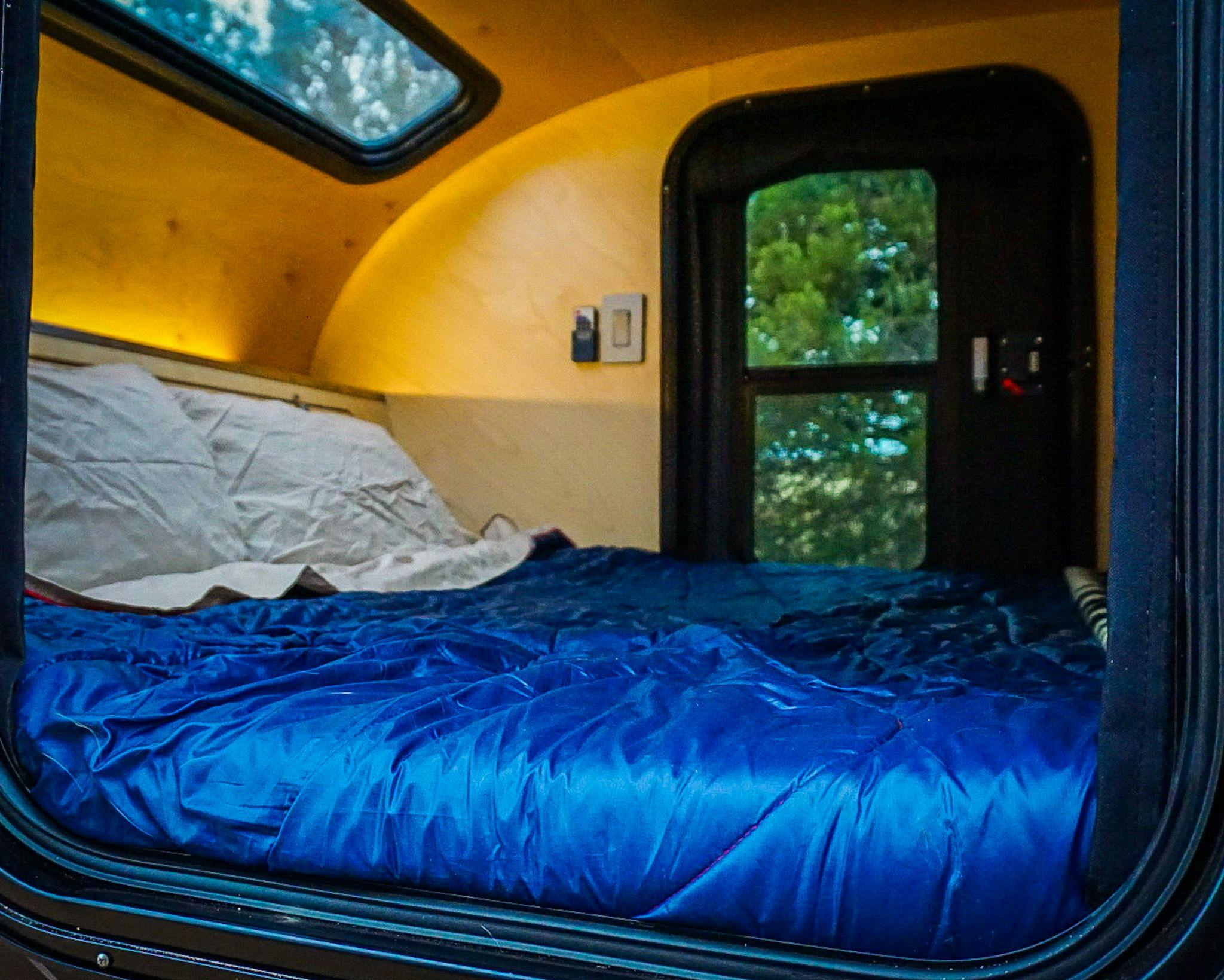 A calming picture displaying the interior of a teardrop trailer with a blue rumpl.