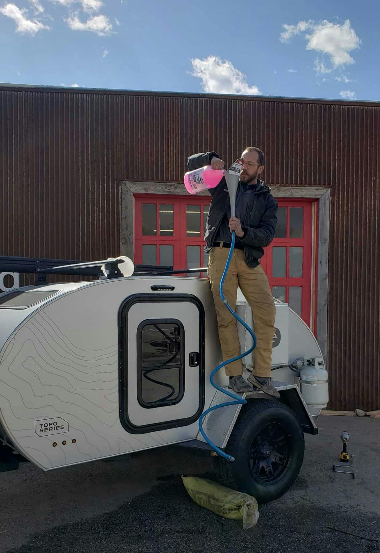 A man pouring antifreeze into an Original TOPO trailer, an adventure camper.