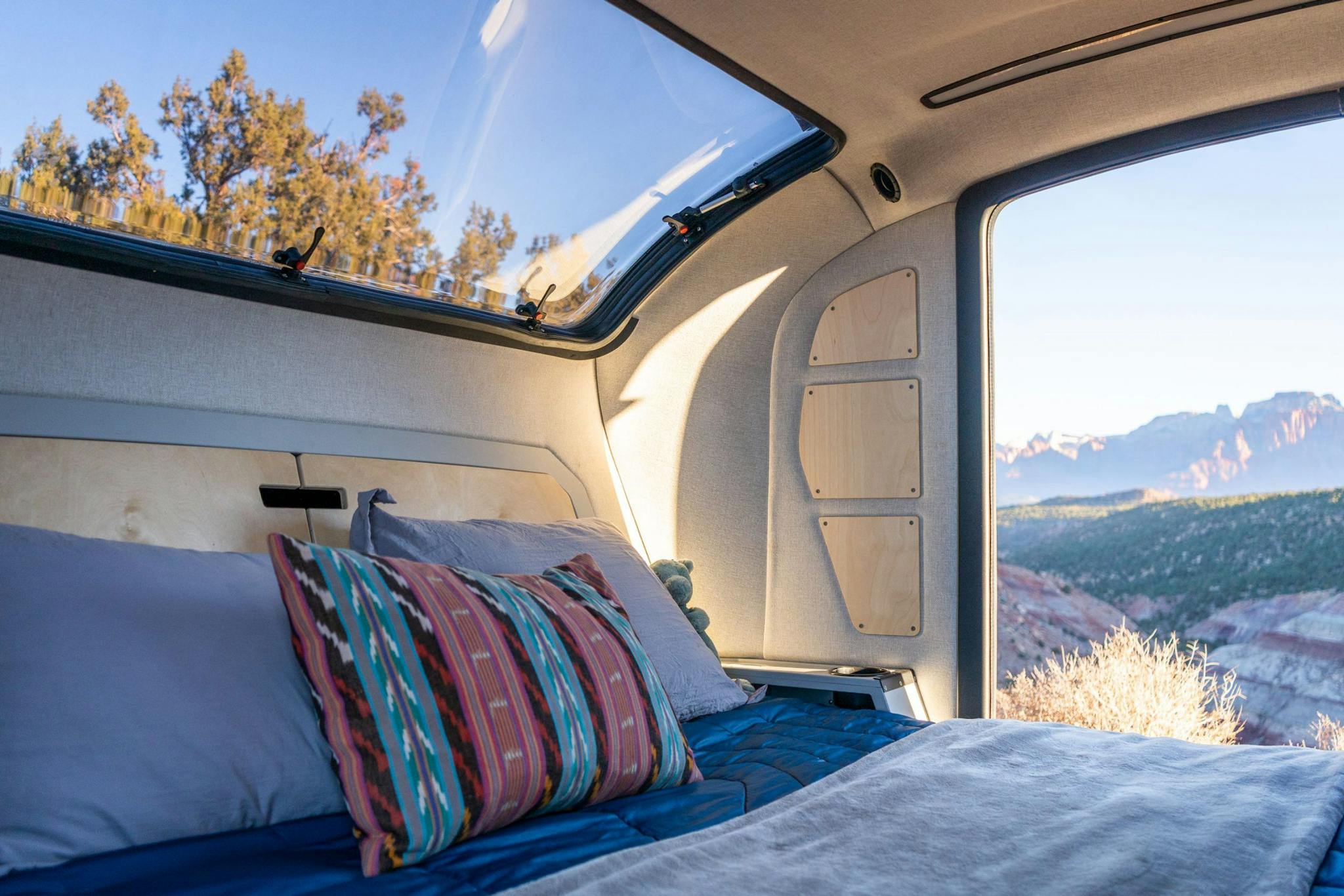The interior of an adventure trailer, showing a beautiful stargazer window and queen sized bed.