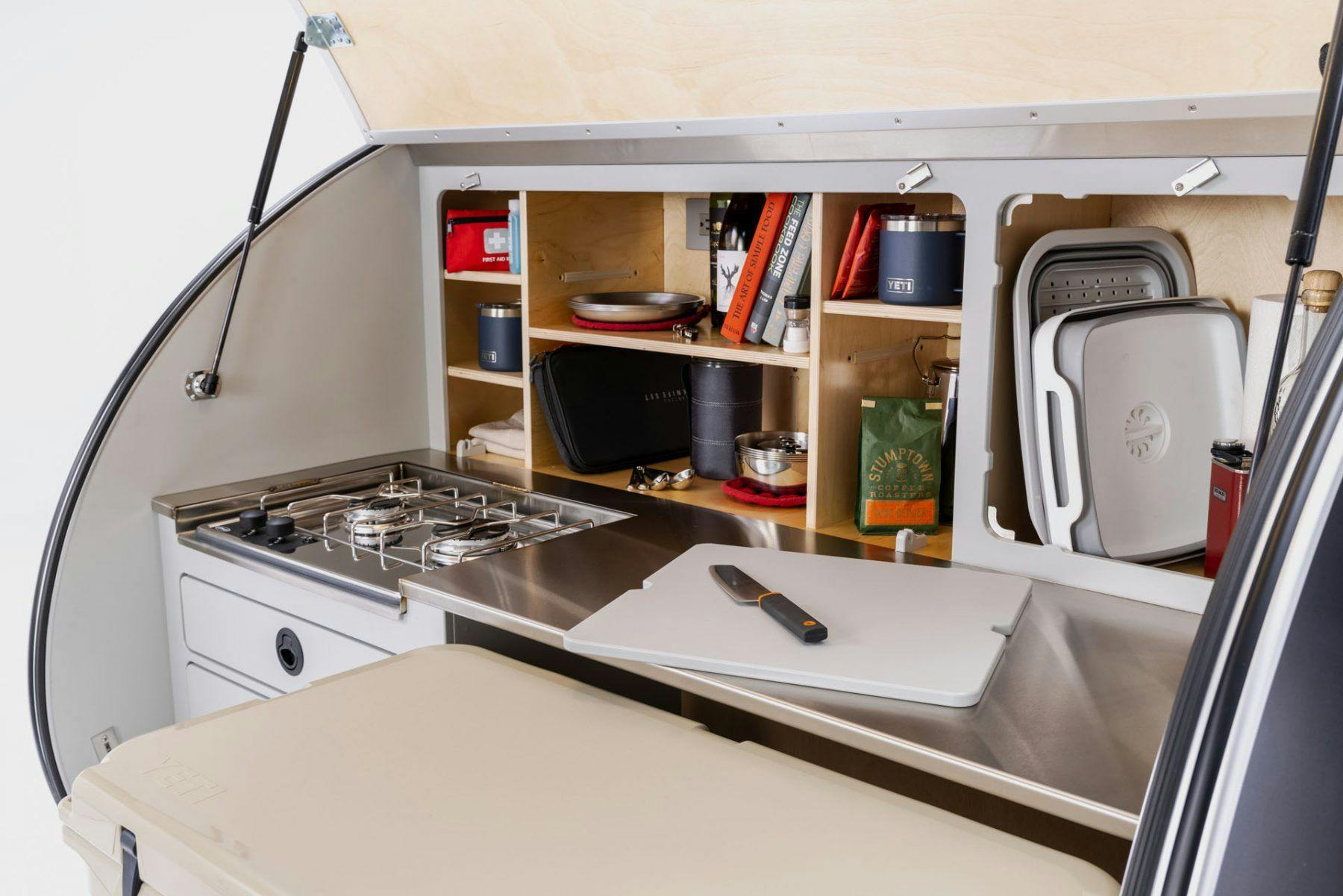 A galley shot of a teardrop camper, showing the storage, stove, and cooler.