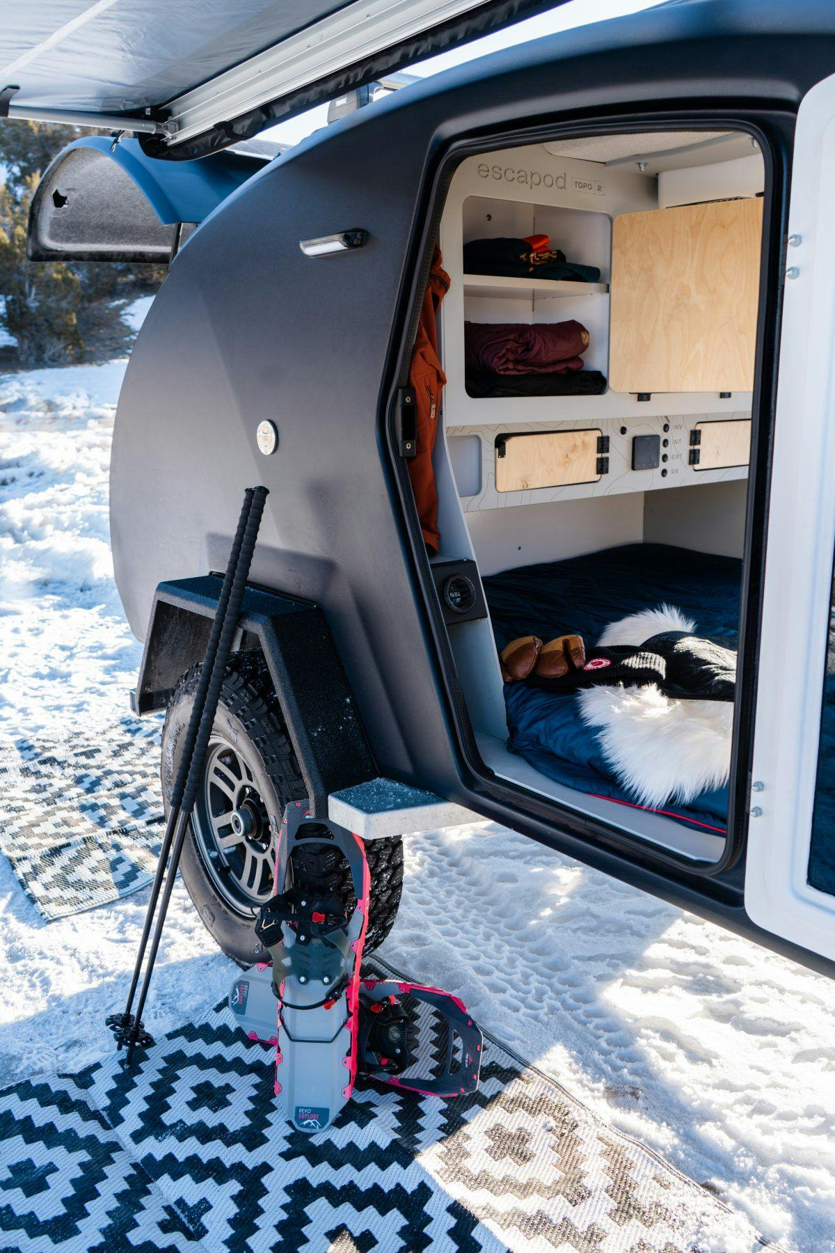 A teardrop camper parked outside in the snow, with snowshoeing gear rested alongside it.