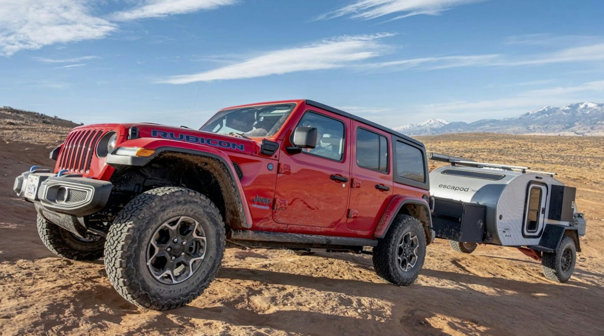 Bright red Jeep Rubicon tows an Escapod up a rocky desert landscape.