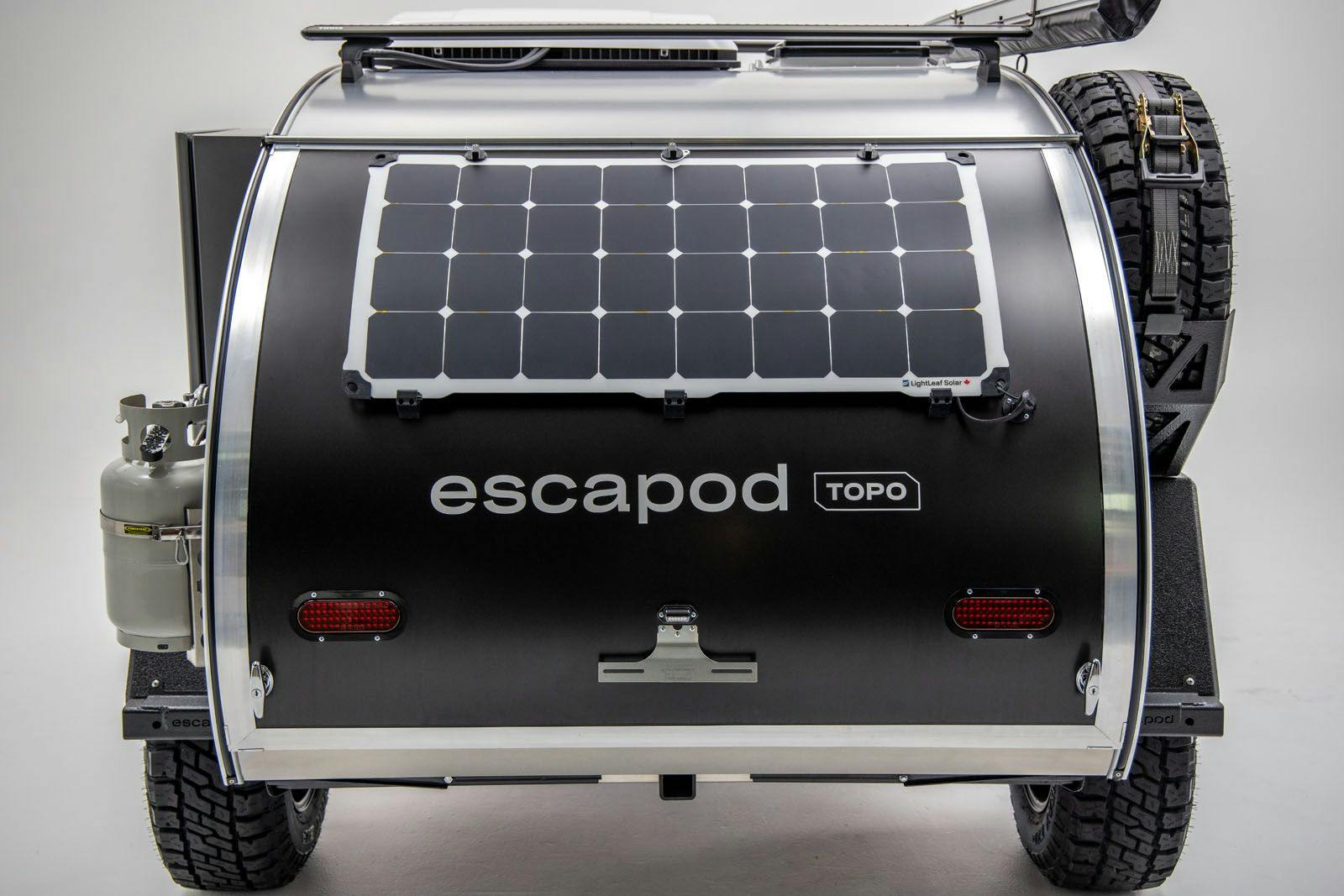A rear shot of a teardrop trailer showing a propane mount, solar panel, and spare tire all mounted to the sides and rear.