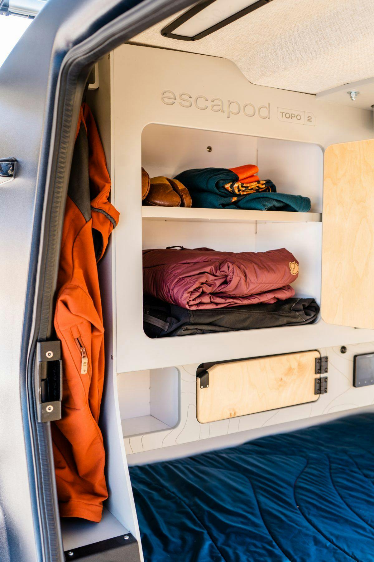 The interior of a teardrop trailer, fully stocked with clothing for a camping trip.