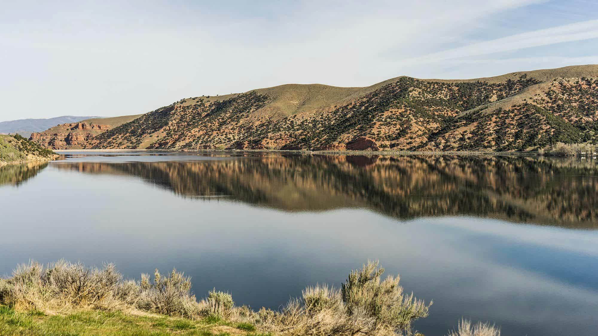 A large reservoir with mountain ranges and trees in the background.