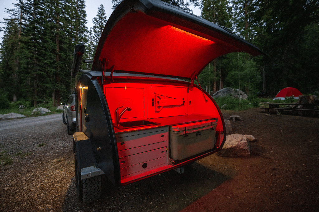 The TOPO2, an offroad trailer, parked in a campground with the galley hatch opened and an LED right light on.