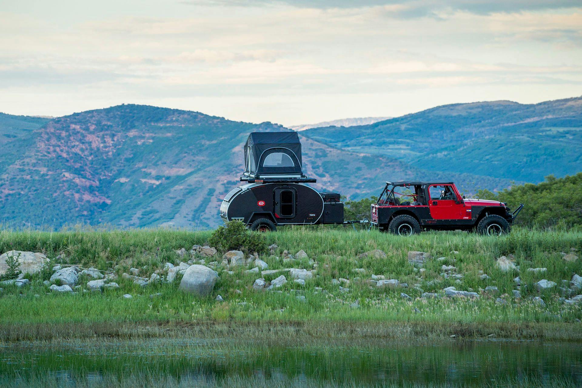 A teardrop trailer being towed by a red JEEP.