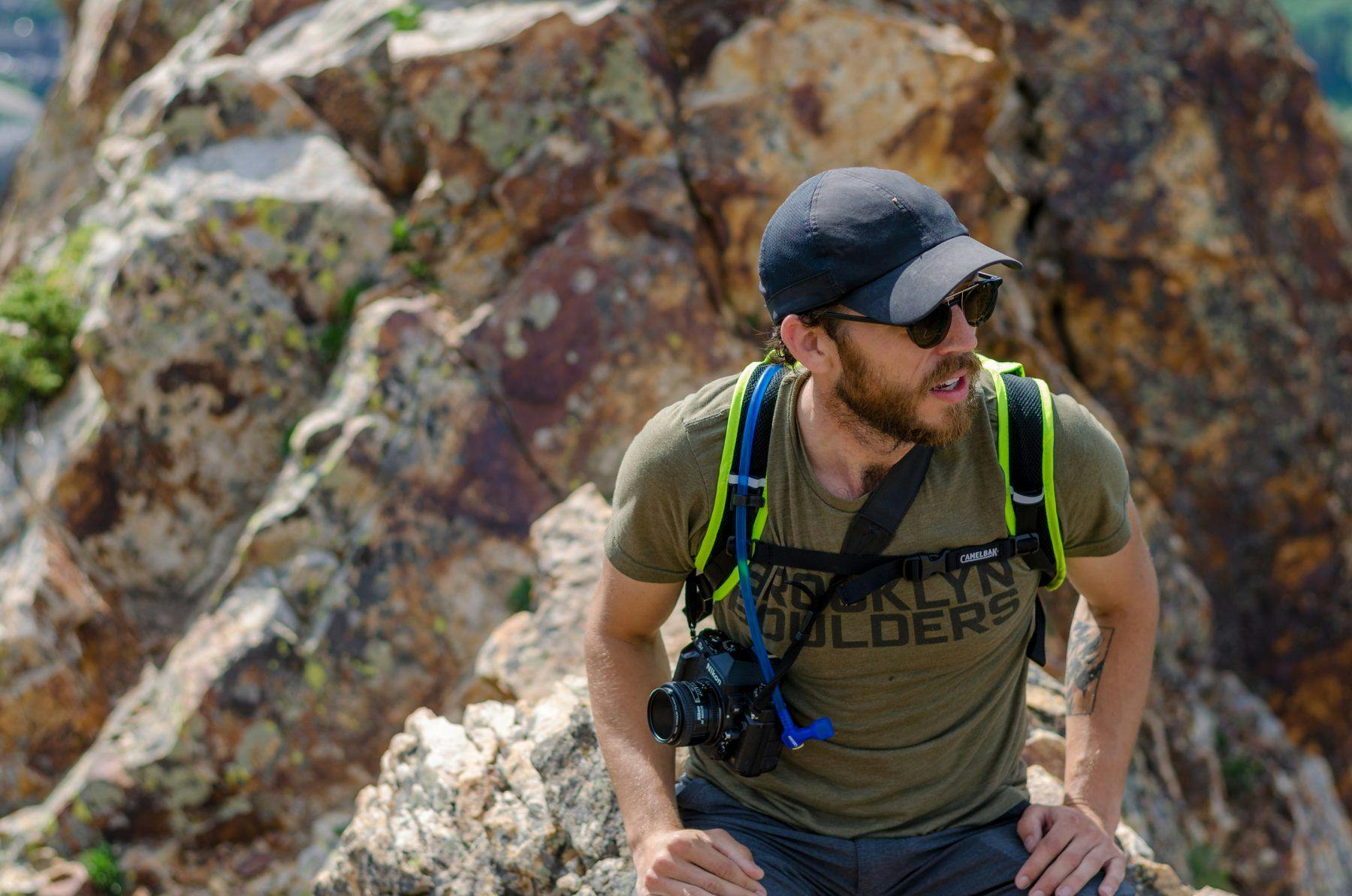 An image of man taking in the scenery at the top of a peak with his camera around his neck.