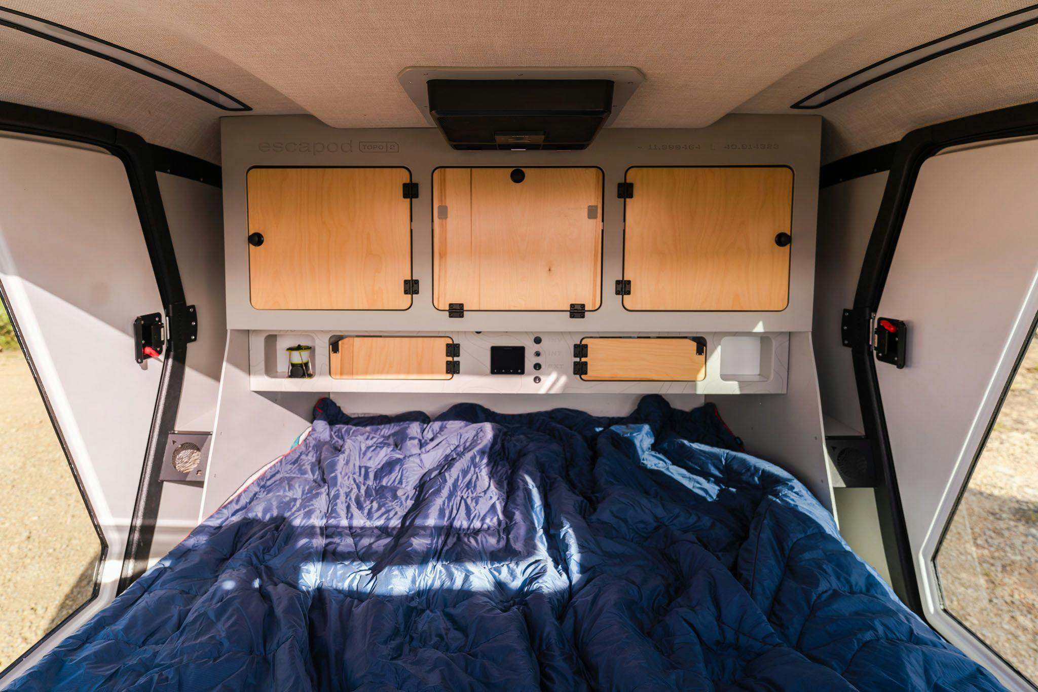 The interior of a teardrop camper, displaying a queen bed, double doors, and a stargazer window