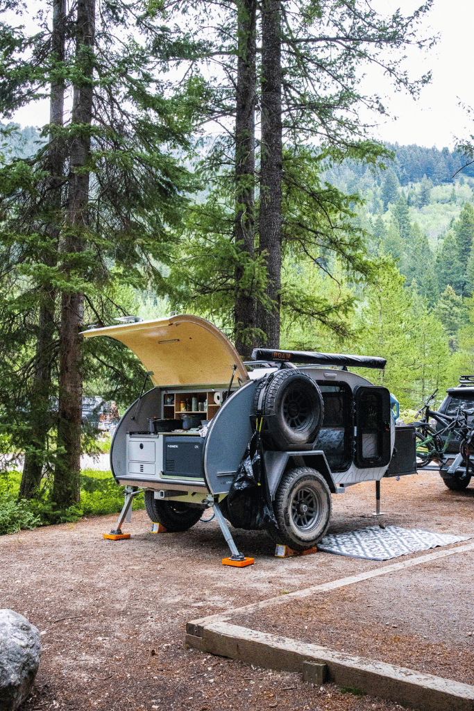 A teardrop trailer set up at camp with the galley open ready for camp cooking.