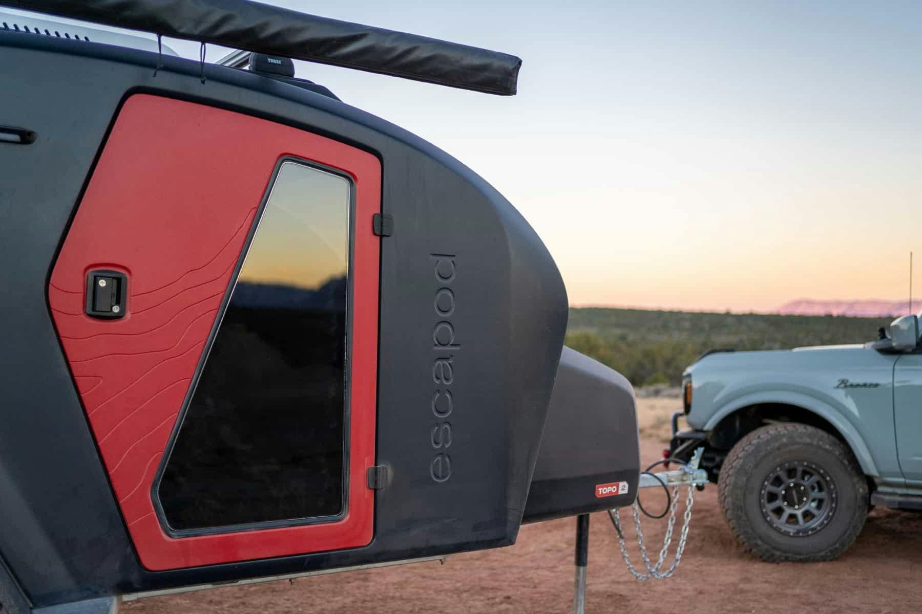 The sunset is reflecting off of the window in a navy blue TOPO2 camping trailer.
