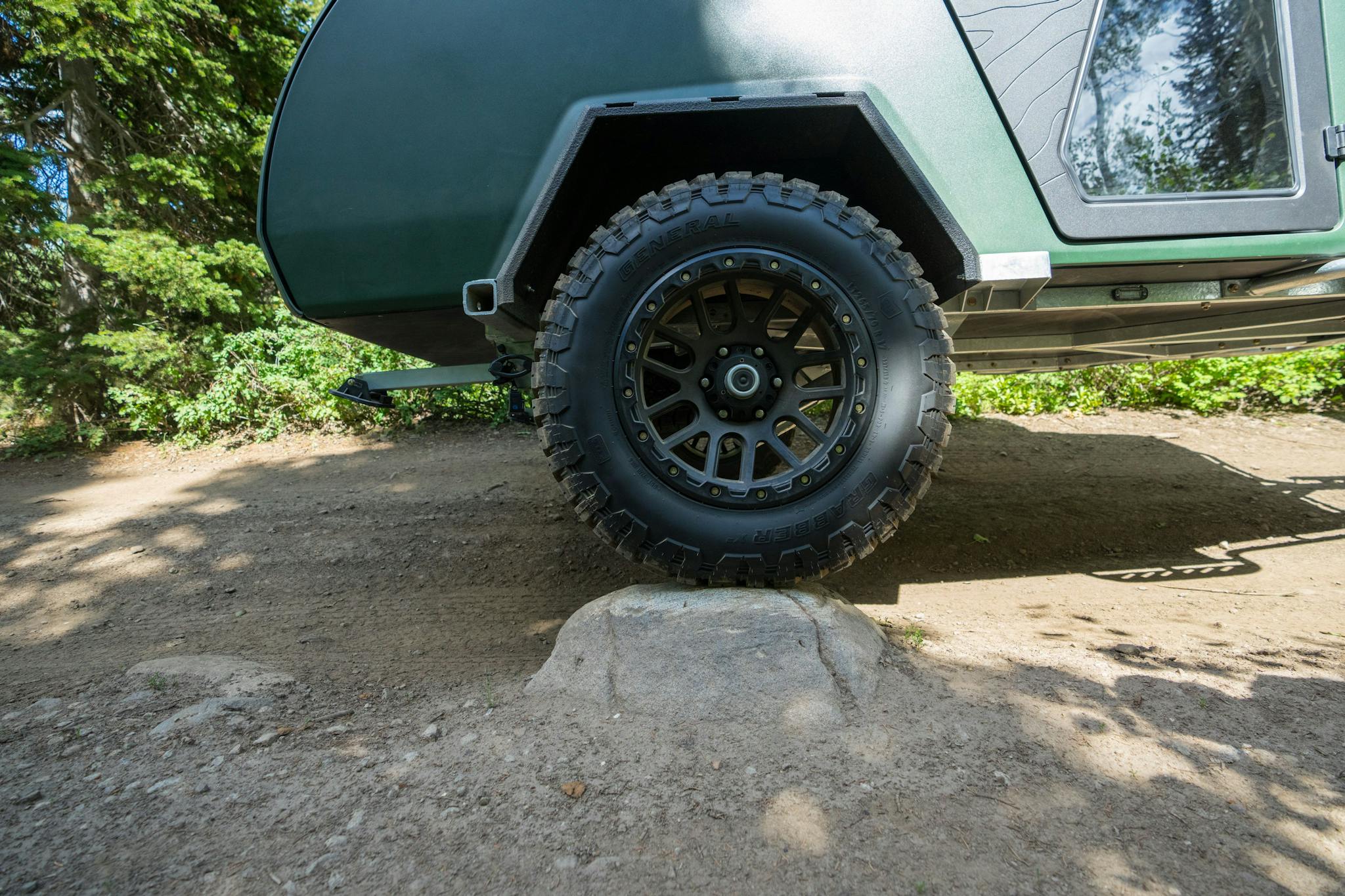 The offroad capability of the TOPO2, an adventure trailer, is on display as is easily rolls over rocks on an offroading trail.