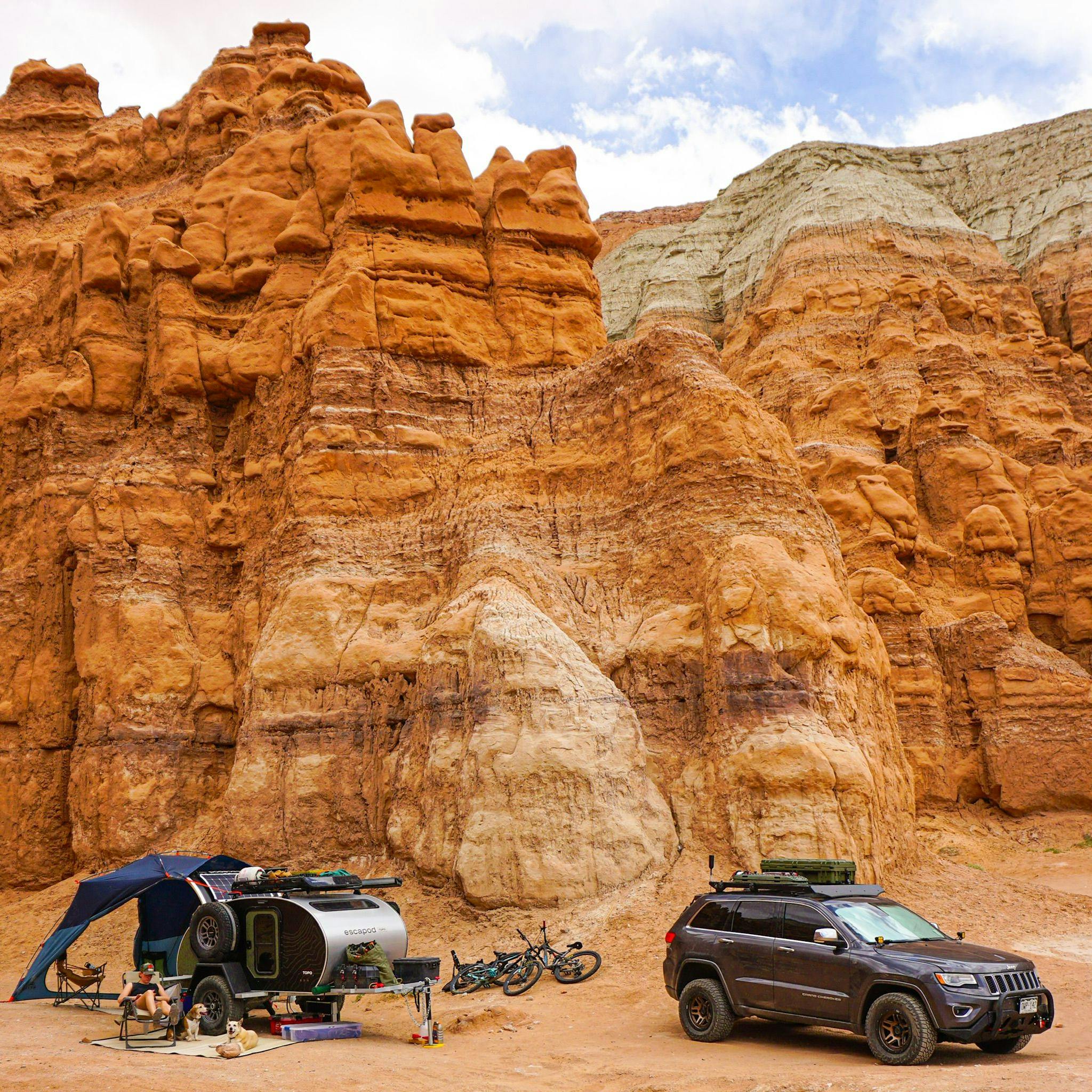 A Jeep towing an Escapod teardrop camper is nestled beneath glowing red rock in Goblin Valley, Utah.