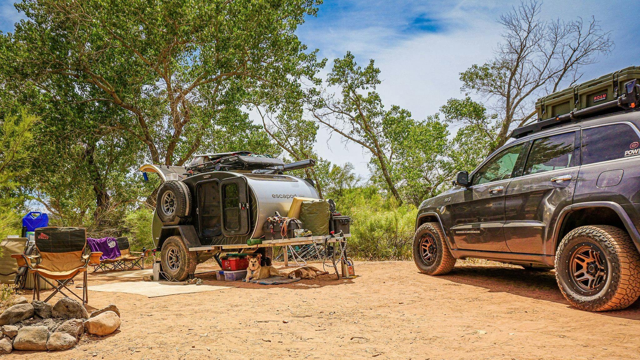 A green and black teardrop trailer parked in a remote camping spot alongside a JEEP.