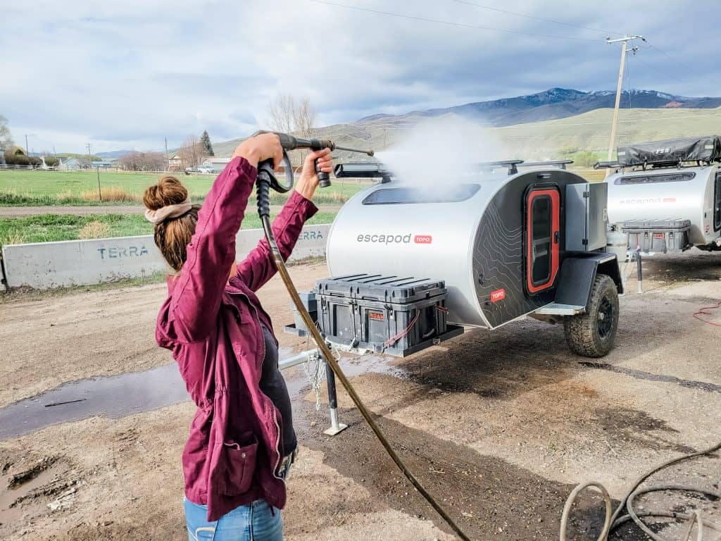 A woman using a hose attachment to spray off her teardrop trailer.
