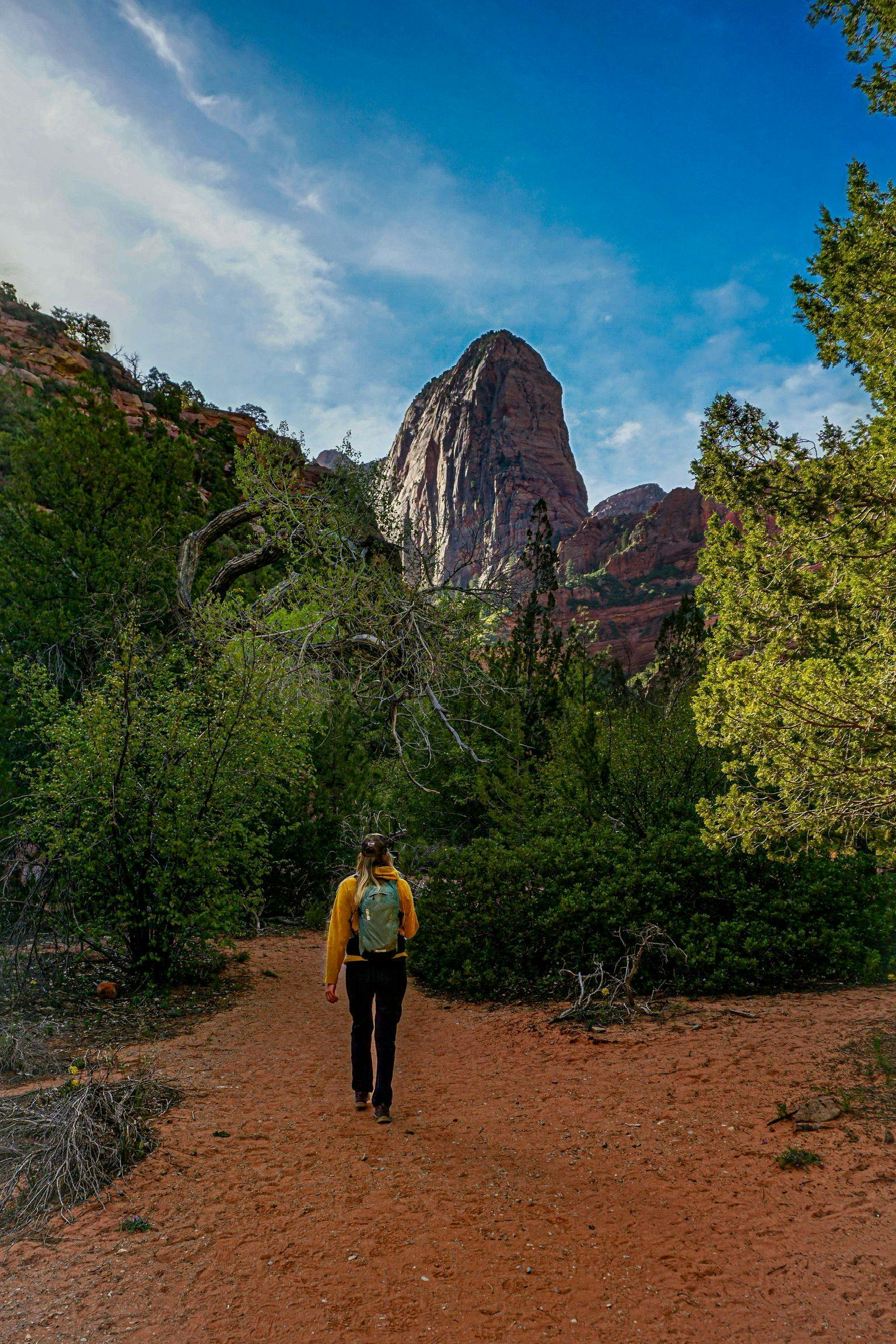 A woman walks on a red sand path toward a glowing granite spire just outside of Zion National Park.