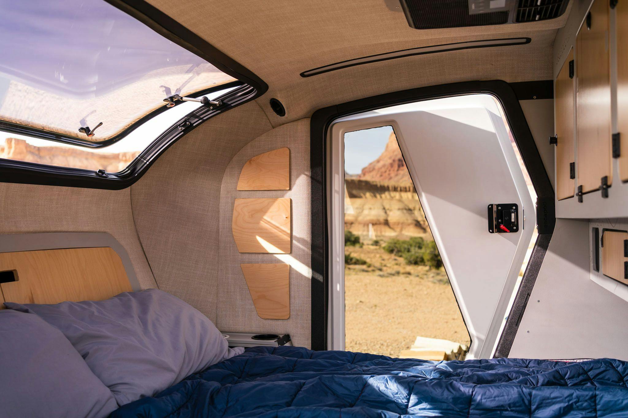 The interior of a teardrop camper, displaying a queen bed, double doors, and a stargazer window
