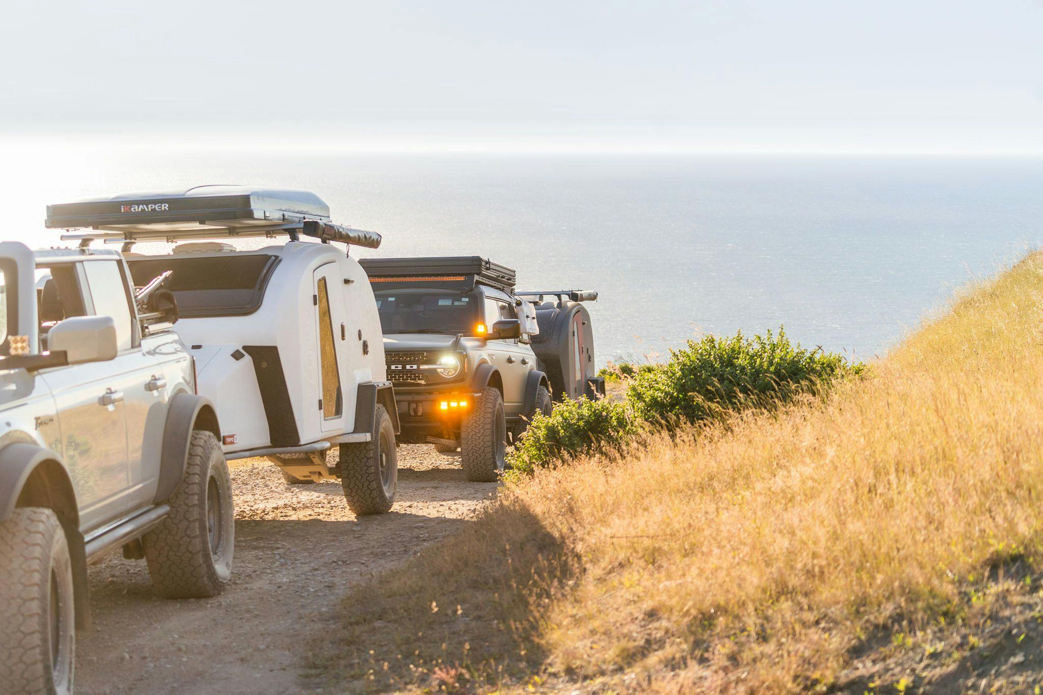 Two TOPO2 Voyagers being towed by Ford Broncos near the beach.