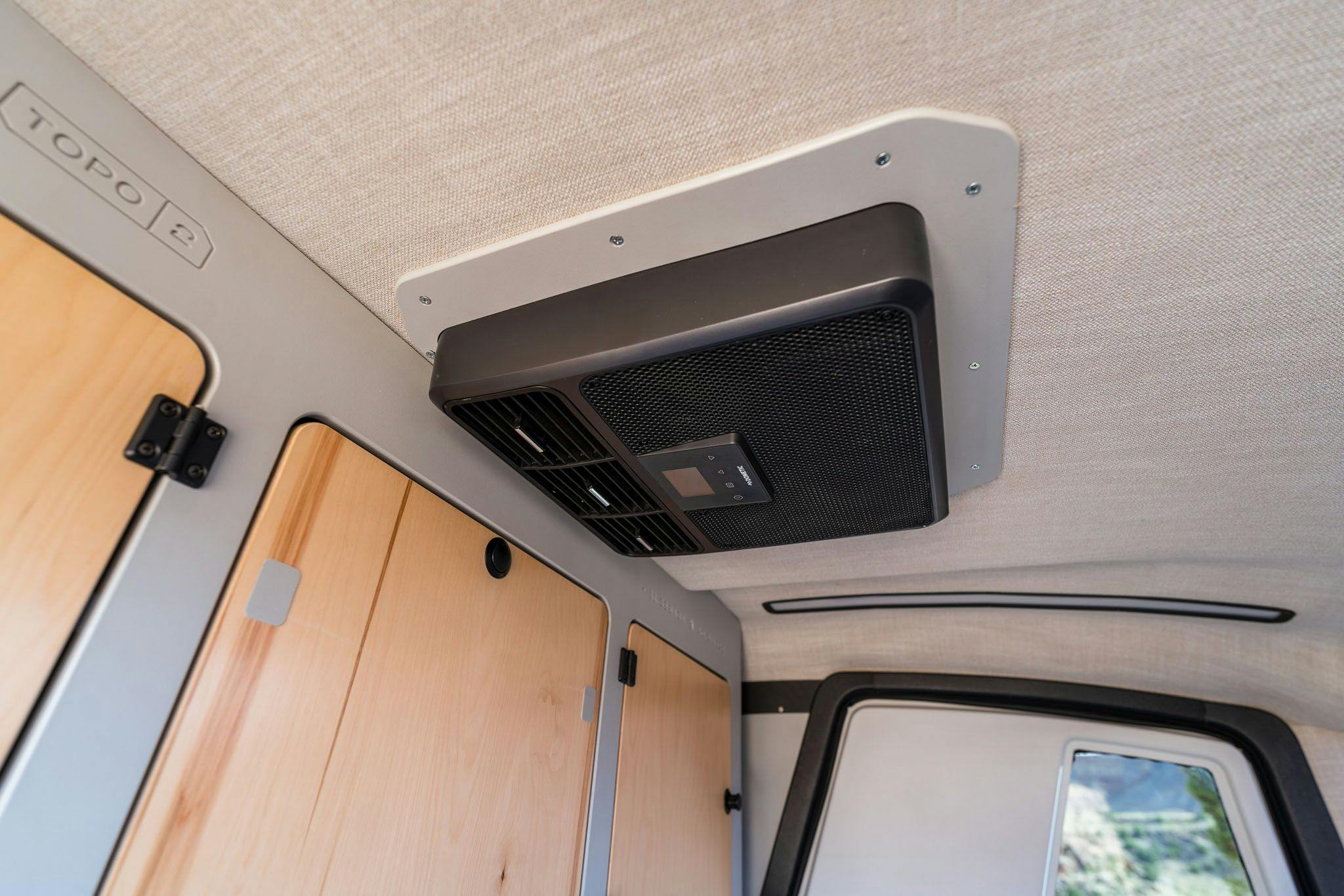 A black air cooling unit mounted into the ceiling of a TOPO2, an offroad teardrop camper.