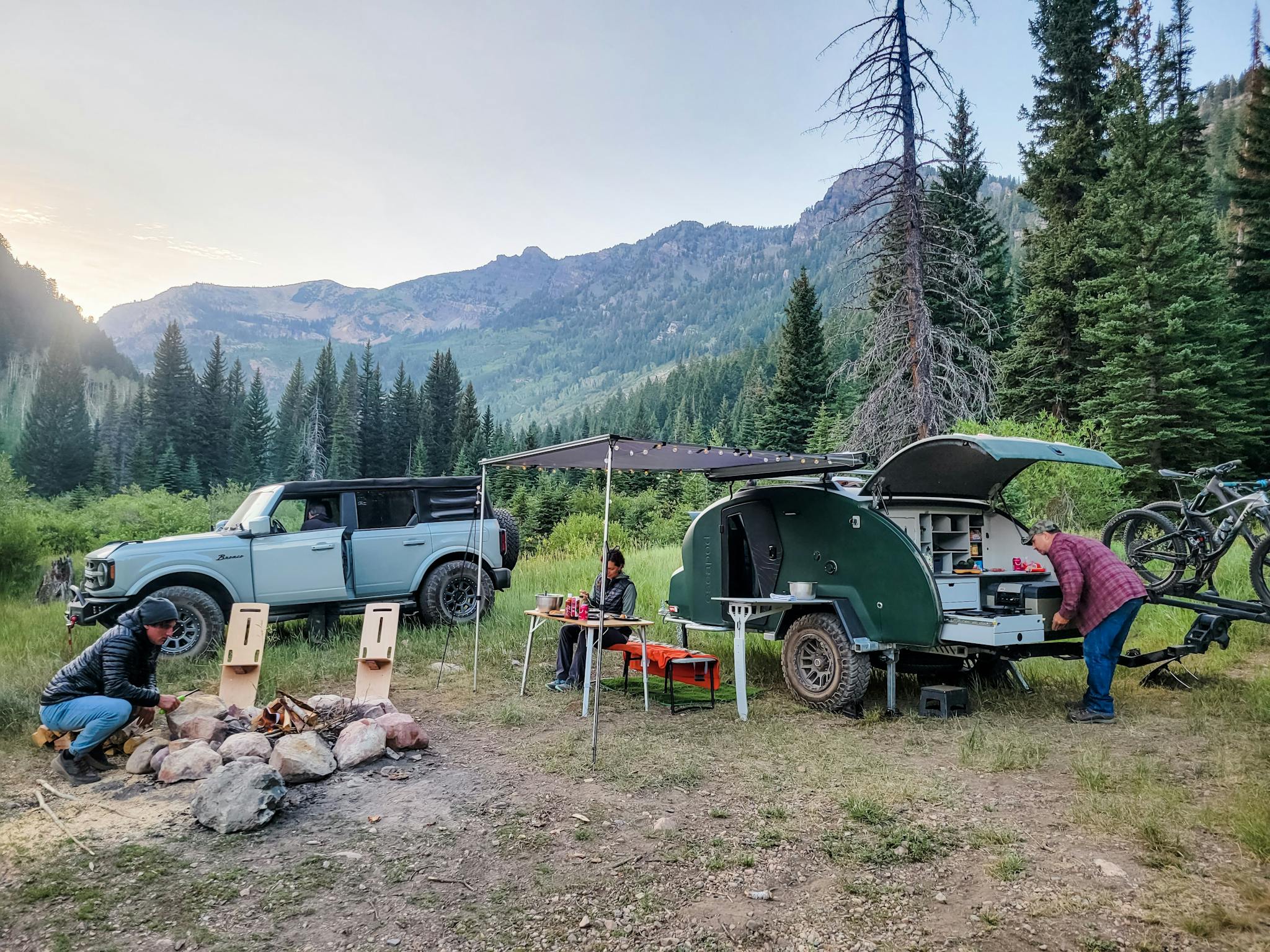 A couple sits enjoying a meal outside of their teardrop camper immersed deep in the mountains of Utah.