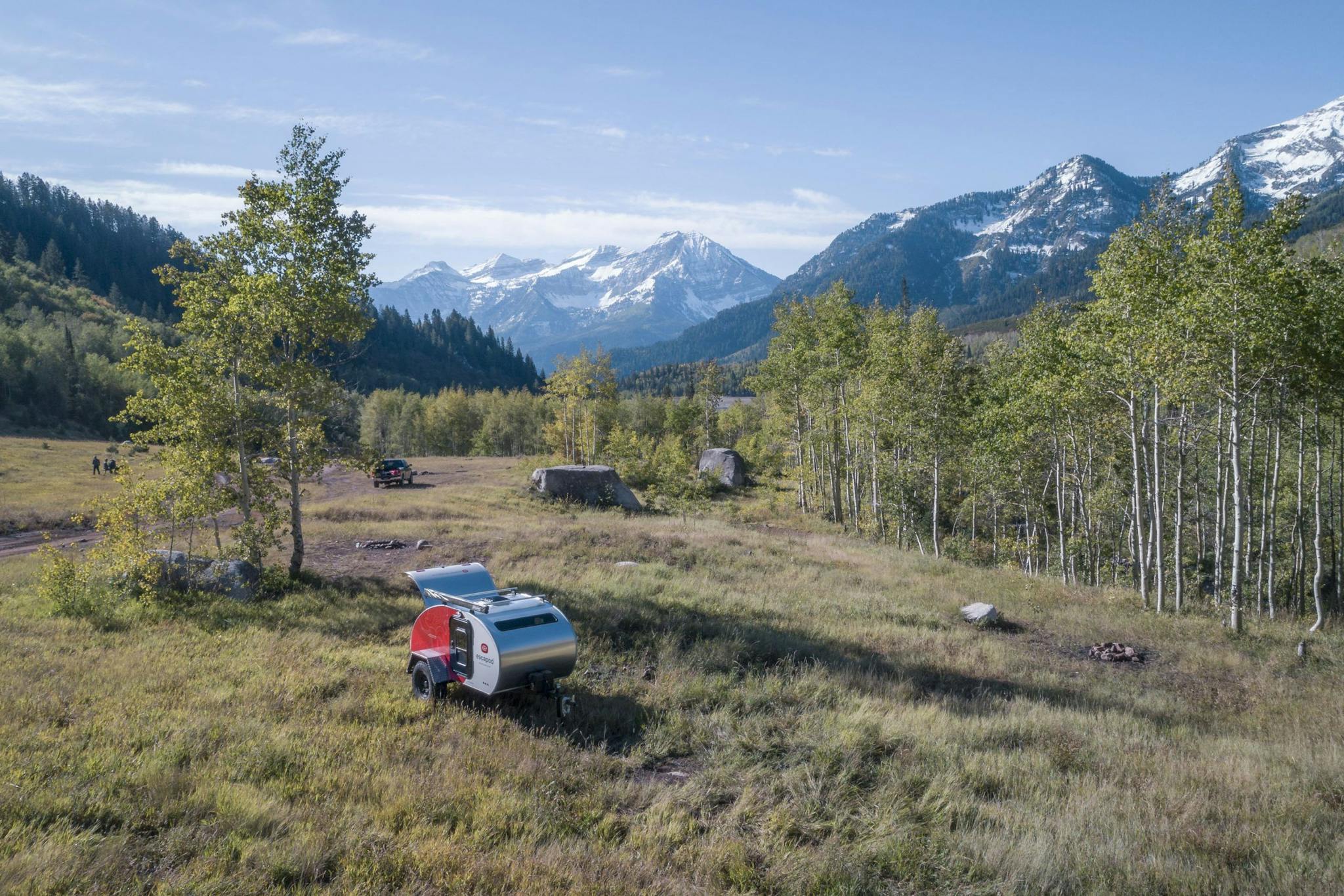 A white and red teardrop camper, in a remote area with trees and mountains in the background.