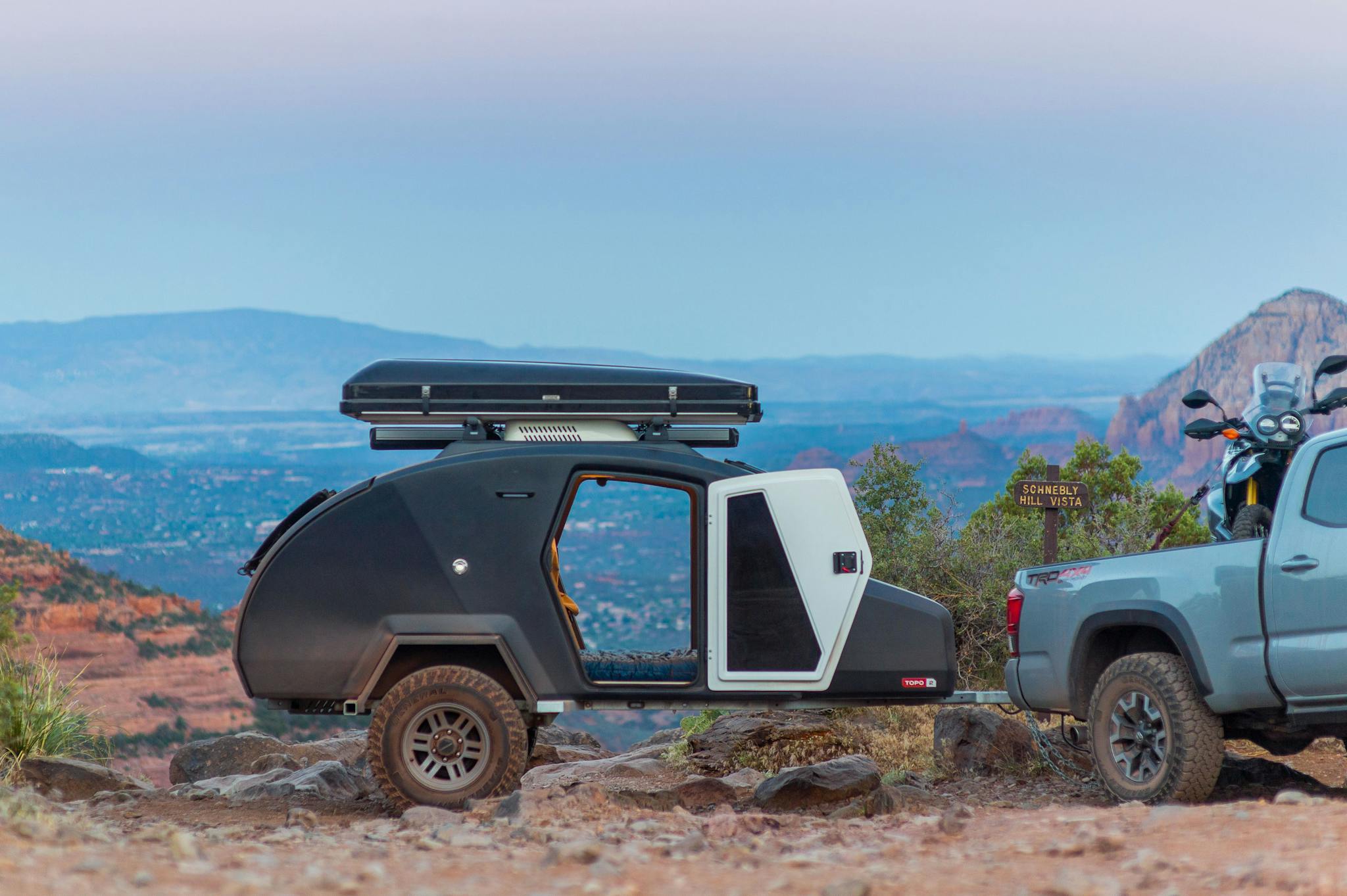 A TOPO2 teardrop camper sits atop Schnebly Hill above Sedona, Arizona at dawn. The doors are open revealing the city below.