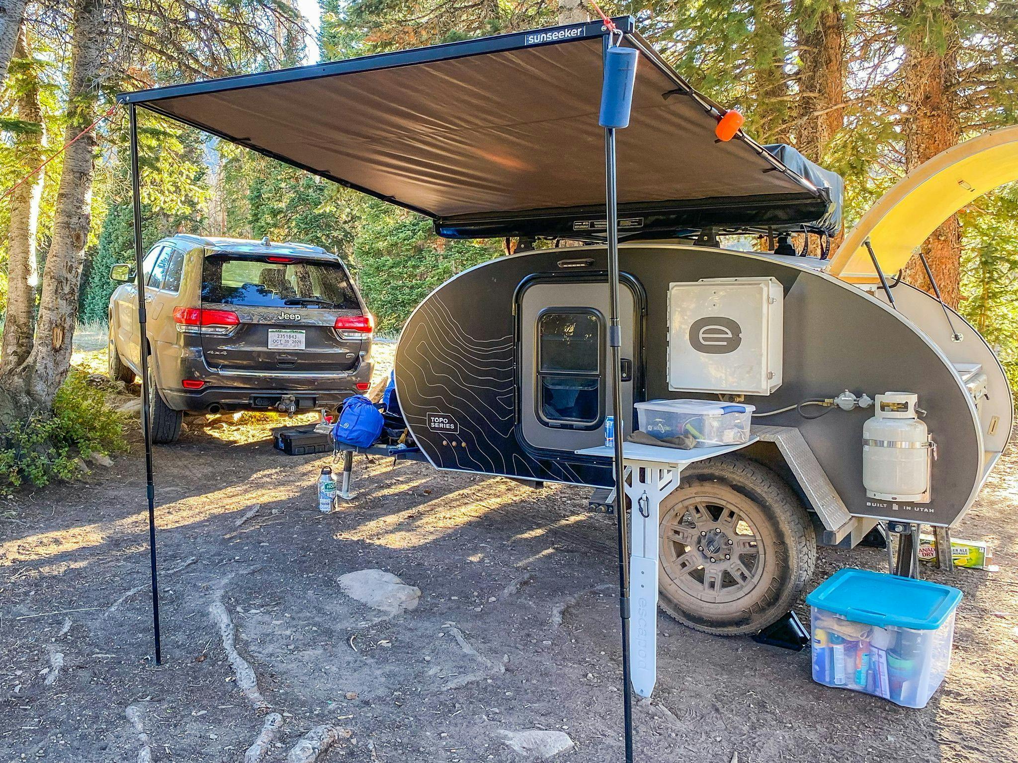 An Escapod teardrop trailer is set up at a camp in Whitney Reservoir. The awning is extended and the hatch is open.
