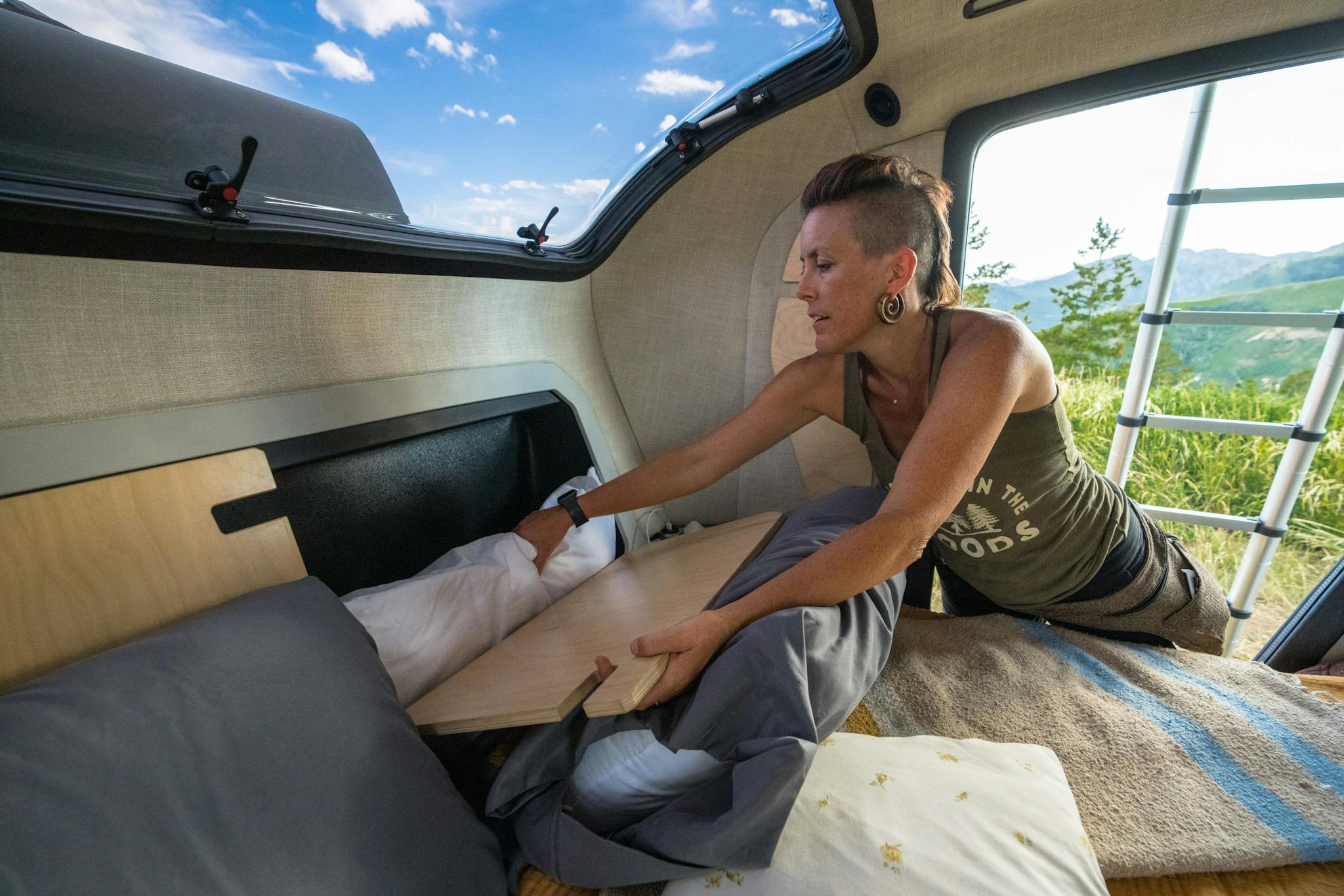 A woman using the storage in her teardrop trailer to store all the camping necessities for their adventure.