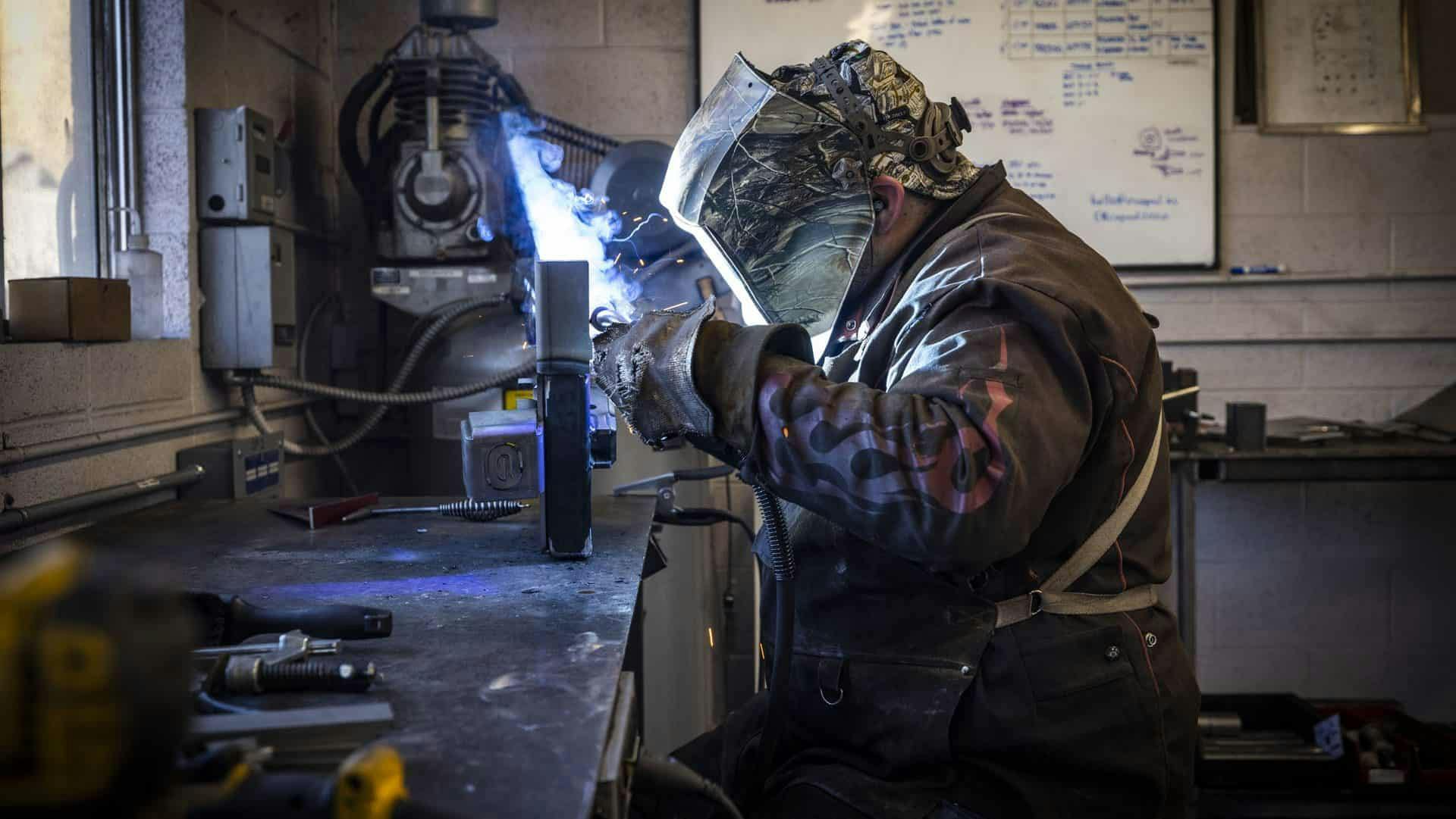 A welder crafting a 2" x 2" steel frame for a teardrop trailer build.